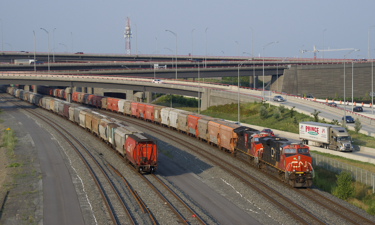 In a rare configuration for this train, potash train CN B730 has a pair of DPU's (CN 3216 & CN 3859) shoving on the rear end as the train passes a cut of parked grain cars.