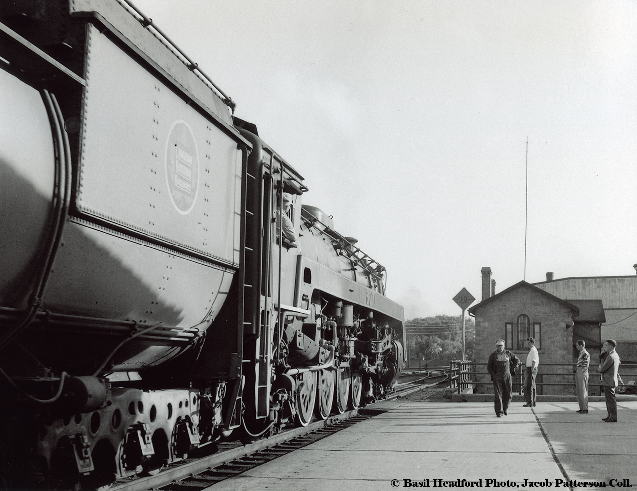 A warm summer evening's passenger stop circa 1959 provides this evening's entertainment for several gentlemen on the platform.  Canadian National Railways U-1-f, 4-8-2, 6071 pauses at Guelph station on the point of train 11 (Toronto - London).  In a short time, the engineer, peering out of the cab, will ease the throttle open and begin the westward journey into the setting sun.  Built by Montreal Locomotive Works in November 1944, 6071 will meet the scrapper's torch in June 1961.Not seen as often as in years past, the human element of railroading and it's community relationships is prominent here.  The engineer in the window, fireman walking the platform, likely headed back to his seat across the cab.  On the platform, a number of locals take in the scene that in a year or so shall be history.  Look close, 2 pairs of father and son make up part of the audience.Departing the station, train 11 will crawl along at the posted 10mph speed limit (note the wooden sign) through the crossover onto the westbound main track.  This northernmost station track would be removed in the 1960s and the platform extended out from the building.  Just beyond the Wyndham Street bridge is Guelph's original police station, built in 1856, along with the original City Hall (1857) which looms in the background.Basil Headford Photo, Jacob Patterson Collection Print.