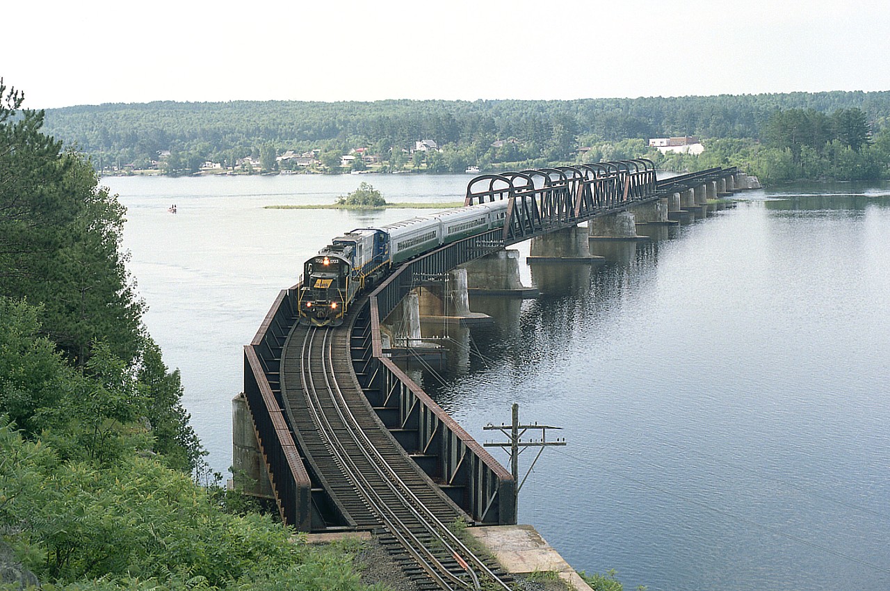 I posted a similar photo to this one some 7 years ago. This image shows more of the surrounding area. I am on the Quebec side of the Ottawa River looking toward the town of Mattawa.  An excursion run, called "The Timber Train" operated out of Mattawa ONT to Temiscaming, QUE briefly over the 1999-2001 years before it shut down. The area was just too remote to reach the number of tourists needed to make this all profitable. Engines on the train are RLK 1703 (GP9E) and 3582 BBD HR412(W). It was sold to Trillium in 2003 after the Excursion Co folded.
The 1703 was scrapped in 2008 and the 3582 is still listed as being on the GIO(Trillium)Holdings roster although I haven't seen it in a long time.