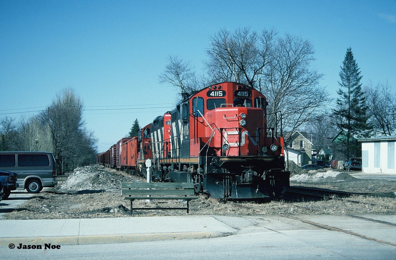 With the rail train now assembled and ready to continue the final movement north, there was one last thing in Palmerston to do and that was simply to eat. The crew of the rail train and other CN workers who had made the trek descended on the town to grab a quick bite at local establishments likely keeping with a tradition that had occurred countless times before. Seen directly at the Main Street crossing or Highway 123 depending how you look at it, CN GP9RM’s 4115 and 4140 and their rail train pause in the heart of Palmerston. 

Today, a Google street view image reveals that a large convenience store and parking lot are now located where the train was photographed, however nearby a nicely painted mural adorns a neighboring building depicting a railway crossing as a fitting tribute to what was once there.