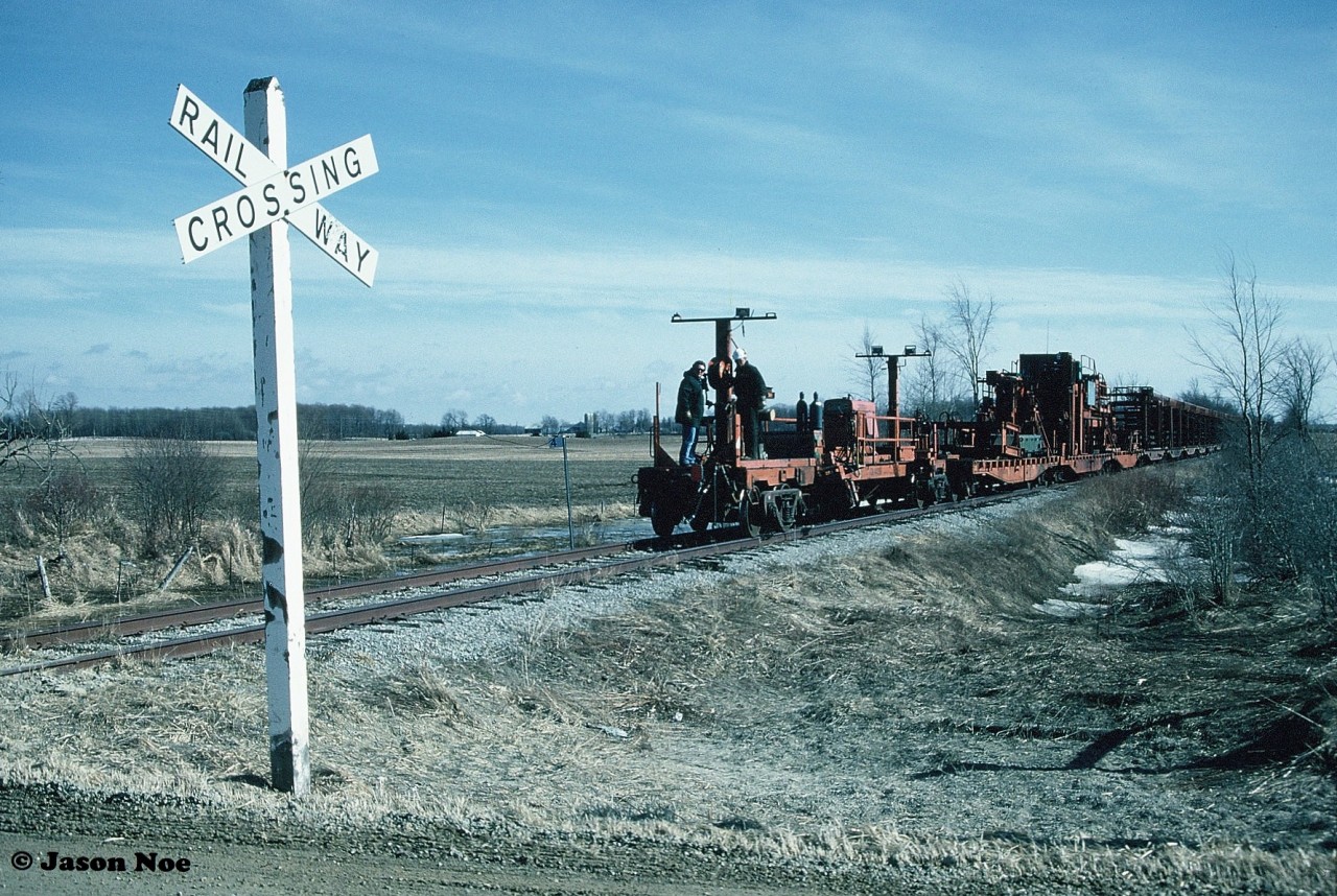 Passing Mile 4 on the Owen Sound Subdivision as it approaches the 7th Line crossing, the CN rail salvage train is viewed just outside the town of Harriston. Having run-around the rail cars at Palmerston, GP9RM’s 4115 and 4140 are shoving the lengthy train the remaining five miles from Palmerston into Harriston where the rail removal process will eventually begin. 

Today this area looks surprisingly similar, minus the crossing signs and rails, as it now is part of the 12.4-kilometer Whites Junction Trail.