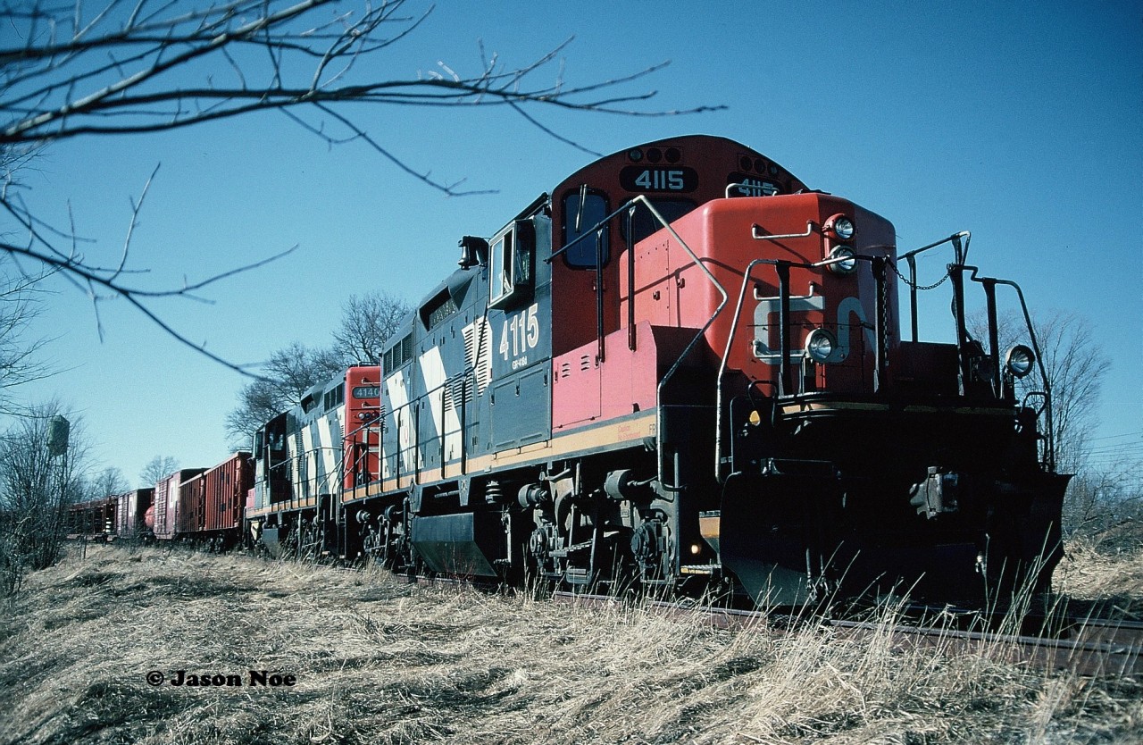 During the afternoon, GP9RM’s 4115 and 4140 with their rail salvage train have finally arrived in the town of Harriston and are seen awaiting instructions from the CN foremen accompanying the crew. The tail-end of the train was at the Raglan Street crossing as the town's old water tower can be seen to the left above the rail cars.
