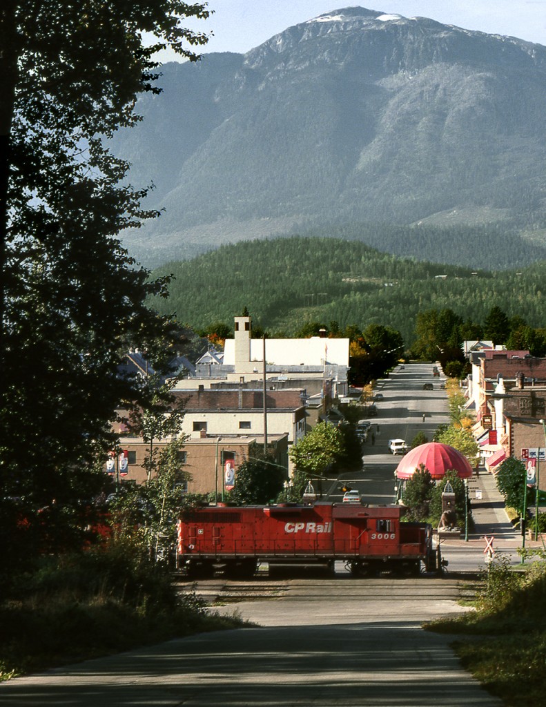 The westbound Shuswap Subdivision wayfreight to Kamloops pulls out of the yard at Revelstoke and crosses MacKenzie Avenue. Mount Begbie oversees the scene