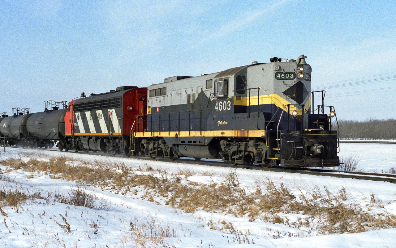 836 heading to the Cold Lake air force base with a solid train of jet fuel tanks. Taken at a farm crossing West of Radway using Konica print film.