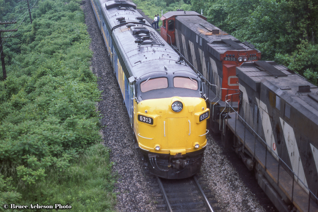 VIA FP9A 6313 adds a nice pop of colour to the scene on this gloomy day at Bayview, where a westbound CN freight led by a pair of M420s has paused for the passage of VIA 72.  M420 2530 leads the freight with crew members on the ground to inspect the passenger equipment.  Originally CN (1) and later VIA 6526, (2) VIA 6313 lives on today, having been sold to the Ohio Central Railway in 2002, and later to Canadian Pacific in 2006 as one of their heritage painted F-units, number 4107.