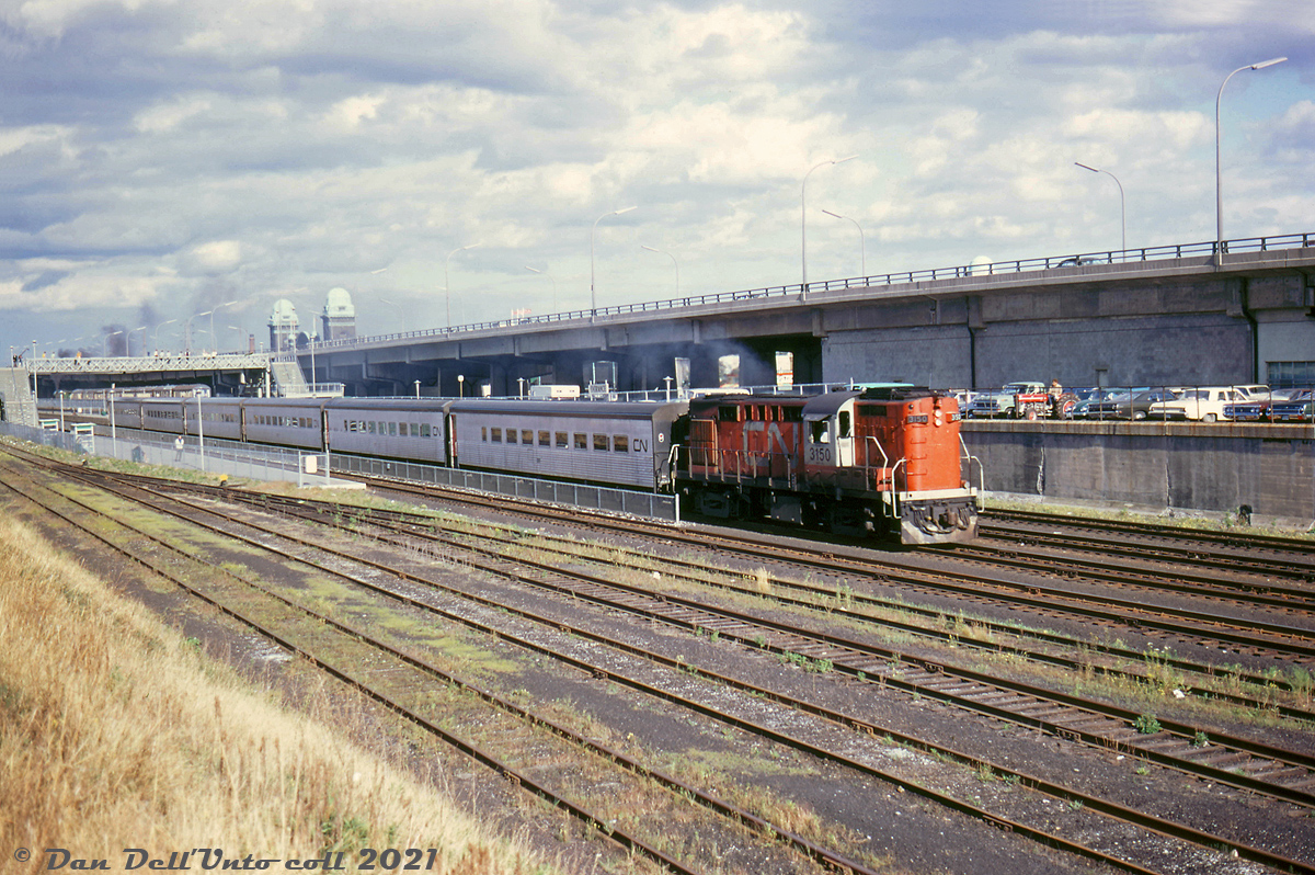 A westbound CN Tempo Train out of Union Station, lead by RS18 3150, speeds through the new Exhibition GO Station on the north passenger main track. Cars from annual fall Canadian National Exhibition patrons pack the parking lot between CN's Oakville Sub rail corridor and the Gardiner Expressway, including a farm tractor (probably not a regular GO commuter)! The top of the CNE's Ricoh Coliseum can be seen in the background.

GO Transit's new Exhibition Station at this spot opened north of the CNE and south of Liberty Village sometime between September 1968 (after the 1968 CNE) and November 1968. The old CN steam-era Exhibition Station to the west at Dufferin Street was briefly used by GO in 1967-1968, but due to the poor setup of the old station handling large seasonal CNE passenger volumes, a new station was built to the east. At the time of this photo, the CNE still had a pair of rail siding of its own to the southeast of the new station for parking rail equipment.

CN Oakville Sub car control diagrams from 1970 show the two middle tracks referred to as passenger mainlines, and the two outer tracks as freight mainlines (presumably used by GO as well). At the bottom are storage tracks for a small CN Strachan yard, at the foot of the Liberty Village industrial area that was still full of sprawling spurs and sidings serving the likes of John Inglis, Canadian General Electric, and Toronto Carpet Manufacturing. This area was referred to in timetables as the "Jefferson Avenue District". Today of course, the area has been highly gentrified with new highrise condos mixed in with old industrial apartment/loft/condo conversions.

Original photographer unknown, Dan Dell'Unto collection slide.
