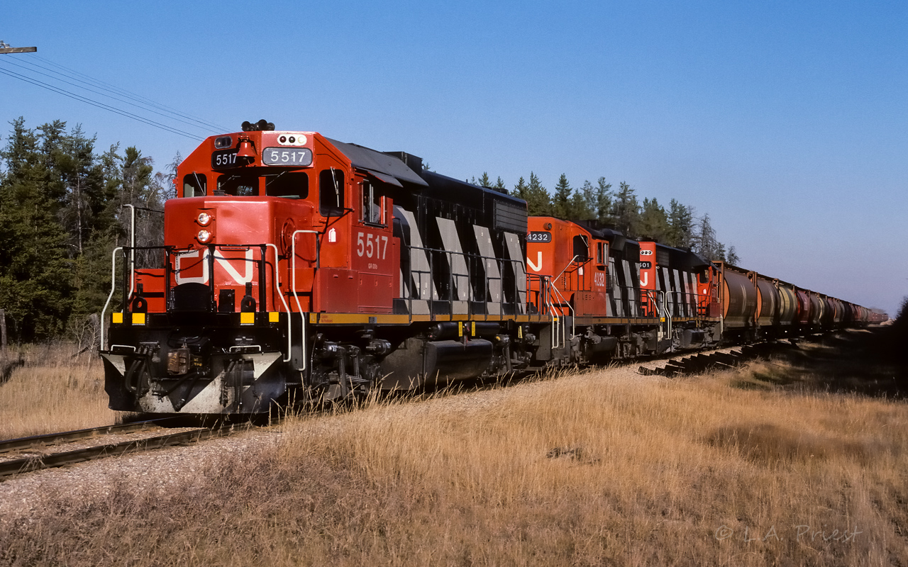 CN 5517 is approaching mile 24.4 with several loads of grain on top of the 30+ sulphur loads further back. Cab 79841 is at the rear. I posted a photo recently of the 5517 from May/85 still in the old CN noodle and black paint. Just over a year later, the new paint is spot on for the sun and blue sky. Taken at approx. 16:00.