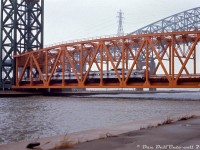 A rainy day down at the Burlington Beach lift bridge finds CN RDC-1's 6106 and 6111 crossing over the Burlington Bay Canal on CN's Beach Subdivision at Hargrove, likely doing a photo run-by for the Upper Canada Railway Society fantrip they're on. CN's Toronto to Niagara Falls Budd "Railiner" RDC runs typically operated through Hamilton via the Oakville-Grimsby Subdivisions, so a pair on the "Beach Branch" wasn't a common occurence. The QEW's Burlington Bay Skyway bridge is visible through the gloom just behind. <br><br> The CN Beach Sub from Burlington to Stoney Creek, originally a through-route for the Hamilton & North Western Railway, was soon severed due to mid-70's QEW freeway construction, and short spurs were operated at each end until abandonment in the early 80's. The tracks that crossed the Burlington Canal lift bridge were replaced with extra traffic lanes. <br><br> <i>Gord Taylor photo, Dan Dell'Unto collection slide.</i> <br><br> Same UCRS fantrip at Stoney Creek: <a href=http://www.railpictures.ca/?attachment_id=43960><b>http://www.railpictures.ca/?attachment_id=43960</b></a><br> 1974 Fantrip with GO power: <a href=http://www.railpictures.ca/?attachment_id=37233><b>http://www.railpictures.ca/?attachment_id=37233</b></a>