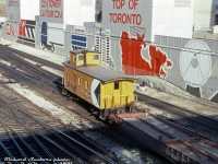 Trailing behind a transfer of piggyback flats lead by rebuilt CP GP9u 1534 (previous photo <a href=http://www.railpictures.ca/?attachment_id=46614><b>here</b></a>), CP wooden caboose 436994 brings up the rear through the John Street interlocking in the downtown Toronto Terminals Railway trackage around Union Station, passing the revised mural at the base of the CN Tower. Lots of old wooden vans (common CP parlance for a caboose) held on until the end of the caboose era in the late 80's, mostly in local, yard and transfer service.<br><br>This particular old steam-era wooden van was originally built in 1941, and is typical of the hundreds CP had on the roster for decades, even well after CP populated its fleet with hundreds of modern steel vans. Sometime around the late 1960's (68-69?) it got the typical plywood modification, where large sheets of plywood were installed on its sides over the old tongue-and-groove wooden siding. Photos show it in Montreal QC in 1968, and then doing time on the Dominion Atlantic Railway (DAR) out east in Nova Scotia during much of the 1970's, and ending its career operating in the Toronto area in the 1980's in local and transfer service, still listed on the roster in 1987 along with many other old wooden vans. It was retired and became a private residence up in Belmore, Ontario in 1991. The Guelph Historical Railway Association (GHRA) eventually acquired and restored 436994 as one of their centerpieces, which including removing the plywood sides and revealing its original wooden exterior. <br><br><i>Richard Sanborn photo, Dan Dell'Unto collection slide (with thanks to Kevin Reed for passing this one on)</i>
