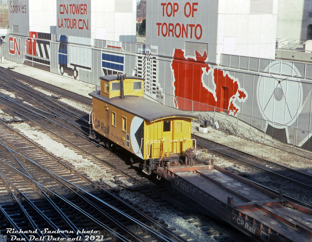 Trailing behind a transfer of piggyback flats lead by rebuilt CP GP9u 1534 (previous photo here), CP wooden caboose 436994 brings up the rear through the John Street interlocking in the downtown Toronto Terminals Railway trackage around Union Station. Lots of old wooden vans (common CP parlance for a caboose) held on until the end of the caboose era in the late 80's, mostly in local, yard and transfer service.

This particular old steam-era wooden van was originally built in 1941, and is typical of the hundreds CP had on the roster for decades, even well after CP populated its fleet with hundreds of modern steel vans. Sometime around the late 1960's (68-69?) it got the typical plywood modification, where large sheets of plywood were installed on its sides over the old tongue-and-groove wooden siding. Photos show it in Montreal QC in 1968, and then doing time on the Dominion Atlantic Railway (DAR) out east in Nova Scotia during much of the 1970's, and ending its career operating in the Toronto area in the 1980's in local and transfer service, still listed on the roster in 1987 along with many other old wooden vans. It was retired and became a private residence up in Belmore, Ontario in 1991. The Guelph Historical Railway Association (GHRA) eventually acquired and restored 436994 as one of their centerpieces, which including removing the plywood sides and revealing its original wooden exterior. 

Richard Sanborn photo, Dan Dell'Unto collection slide (with thanks to Kevin Reed for passing this one on)