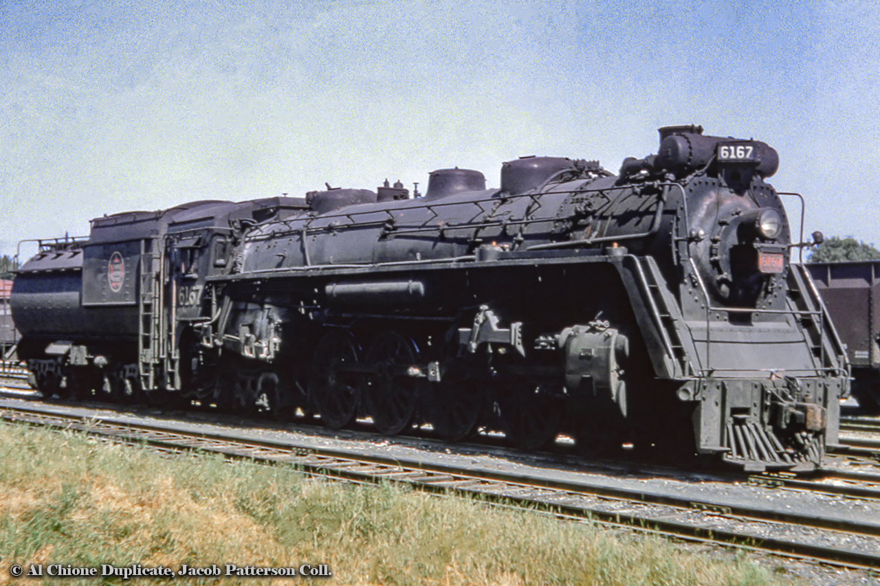 CNR 6167 is seen here in Guelph's XV yard, cold and dead during it's first retirement.  Note the main rod laying on the running board.  Within the year, the crews at CNR's Stratford Shops will get to work overhauling the engine for use on excursion trips, turning her out looking as good as new.  Almost a year to the day later on July 10, 1960, 6167 can be seen on one of the first excursions at Niagara Falls.Having spent most of her career (1940 - 1959) based out of Turcot Yard in Montreal in the passenger pool, operating east to the Maritimes, 6167 had been transferred to the Mimico freight pool early in 1959 (note all black, no white grab irons or whitewalls) and retired a few months later*.  Her excursion service would cover 1960 - 1964, logging over 1 million miles.  *Information per John Mills.Original Photographer Unknown, Al Chione Duplicate, Jacob Patterson Collection Slide.