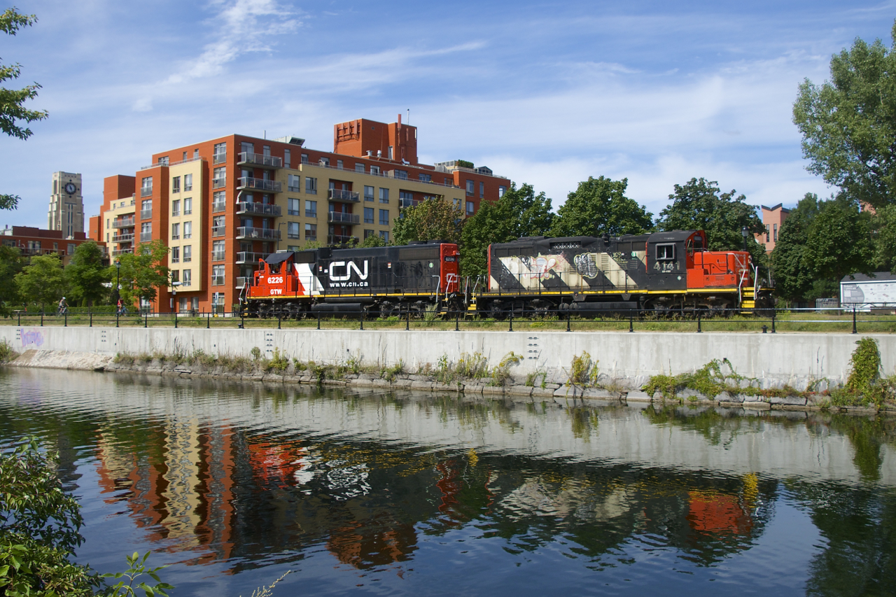 GTW 6262 & CN 4141 are casting a bit of a reflection in the Lachine Canal as they head back to the main line after dropping off six grain cars at Ardent Mills. At far left is the Atwater Market tower. The Atwater Market opened in 1933 and is still a popular location for purchasing fresh foods.