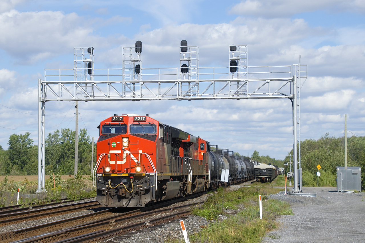 CN 585 has CN 3217, CN 3864 and 58 cars as it passes a signal bridge located where the CN Kingston Sub goes from four to two tracks. At right cars are stored on Track 4.