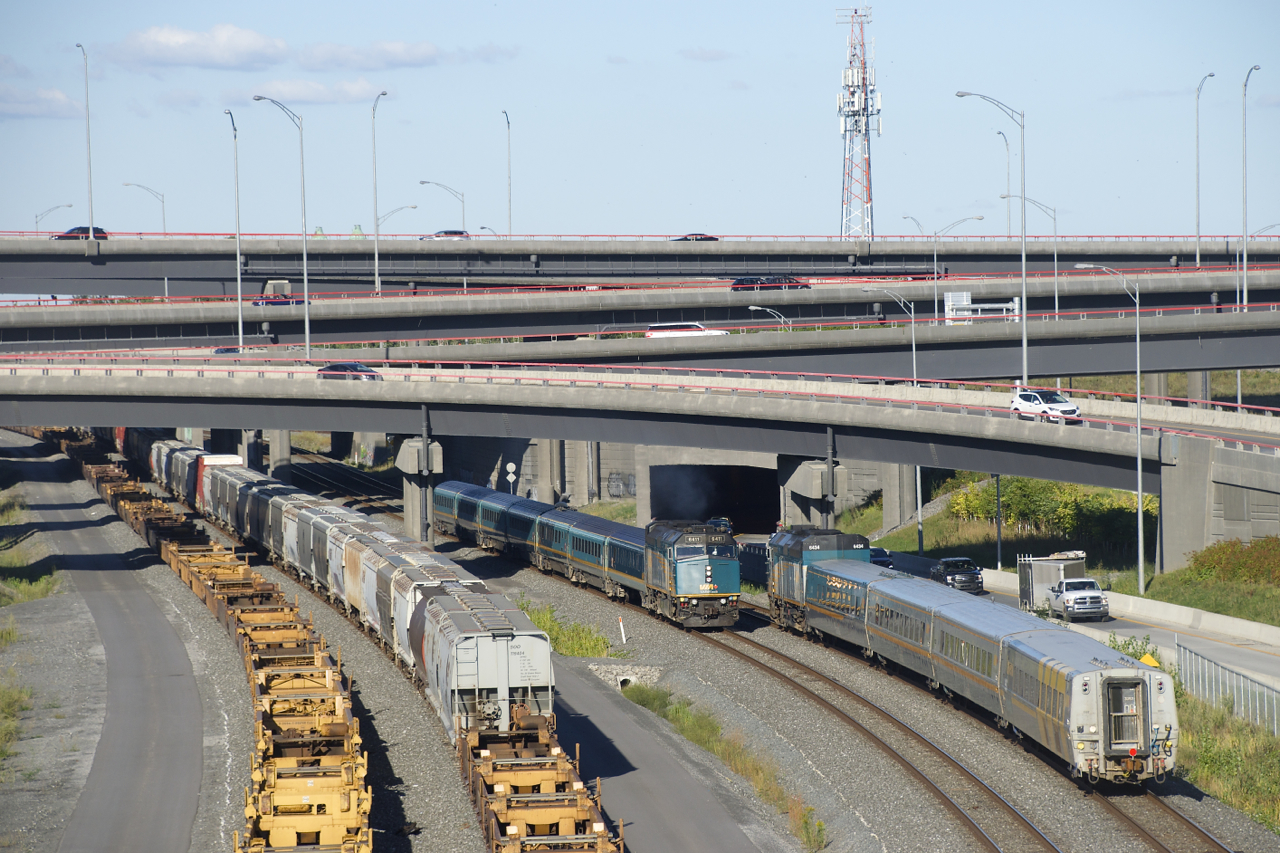 VIA 37 with VIA 6411 and a Renaissance set is meeting VIA 64 with VIA 6434 and an LRC set at speed by the Turcot Interchange. At left are stored cars on track 29 and the freight track of the CN Montreal Sub.