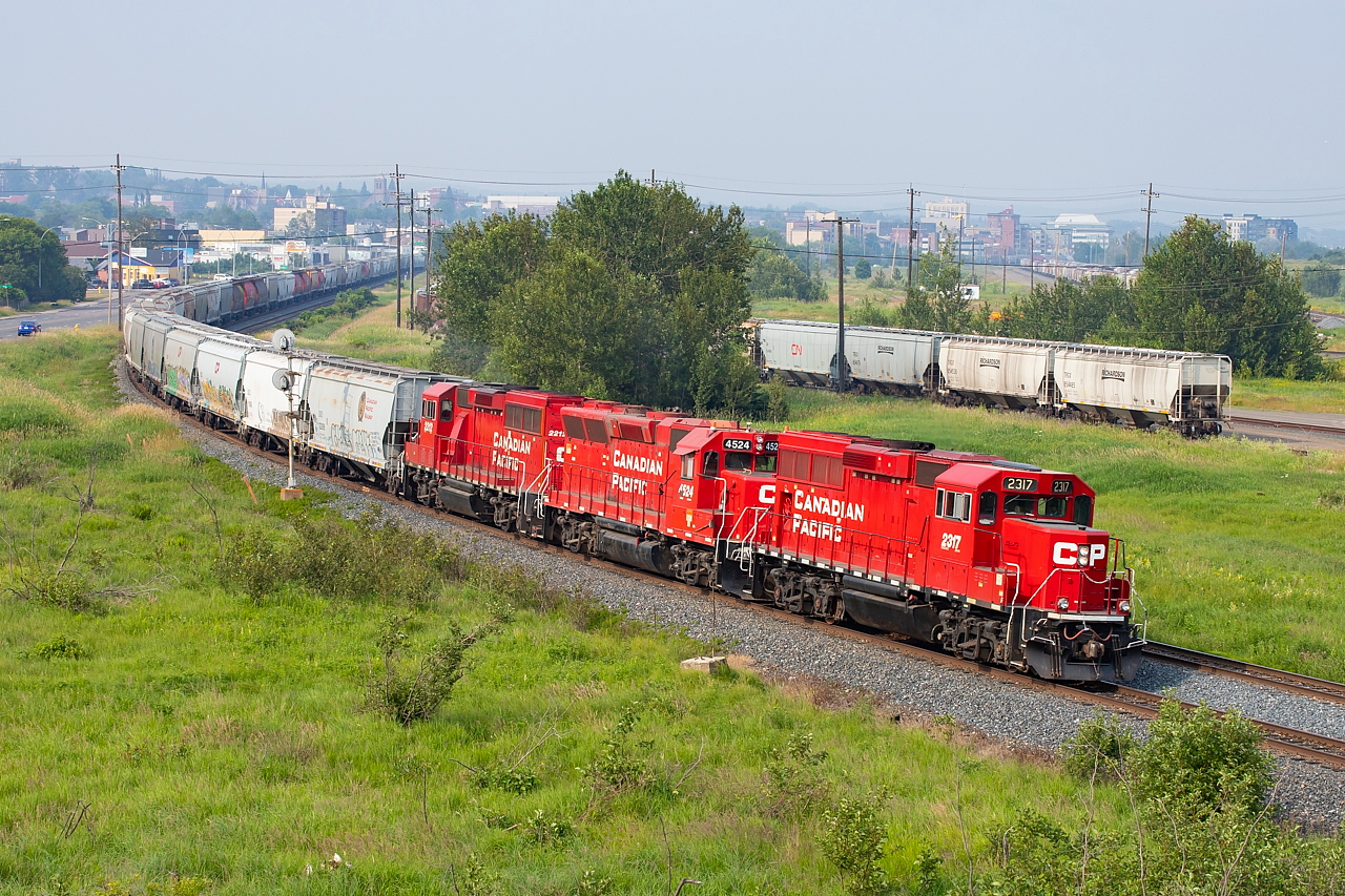 The sun is doing its best to fight through drifting forest fire smoke as CP 2317 leads for the 1559 Yard Job as they head westbound on the north track of the Nipigon Sub with a pull of empties from the Richardson elevator in the Current River area of Thunder Bay. The signal protects the diamond with the CN Kashabowie Sub, movements over which are controlled by CN RTC.