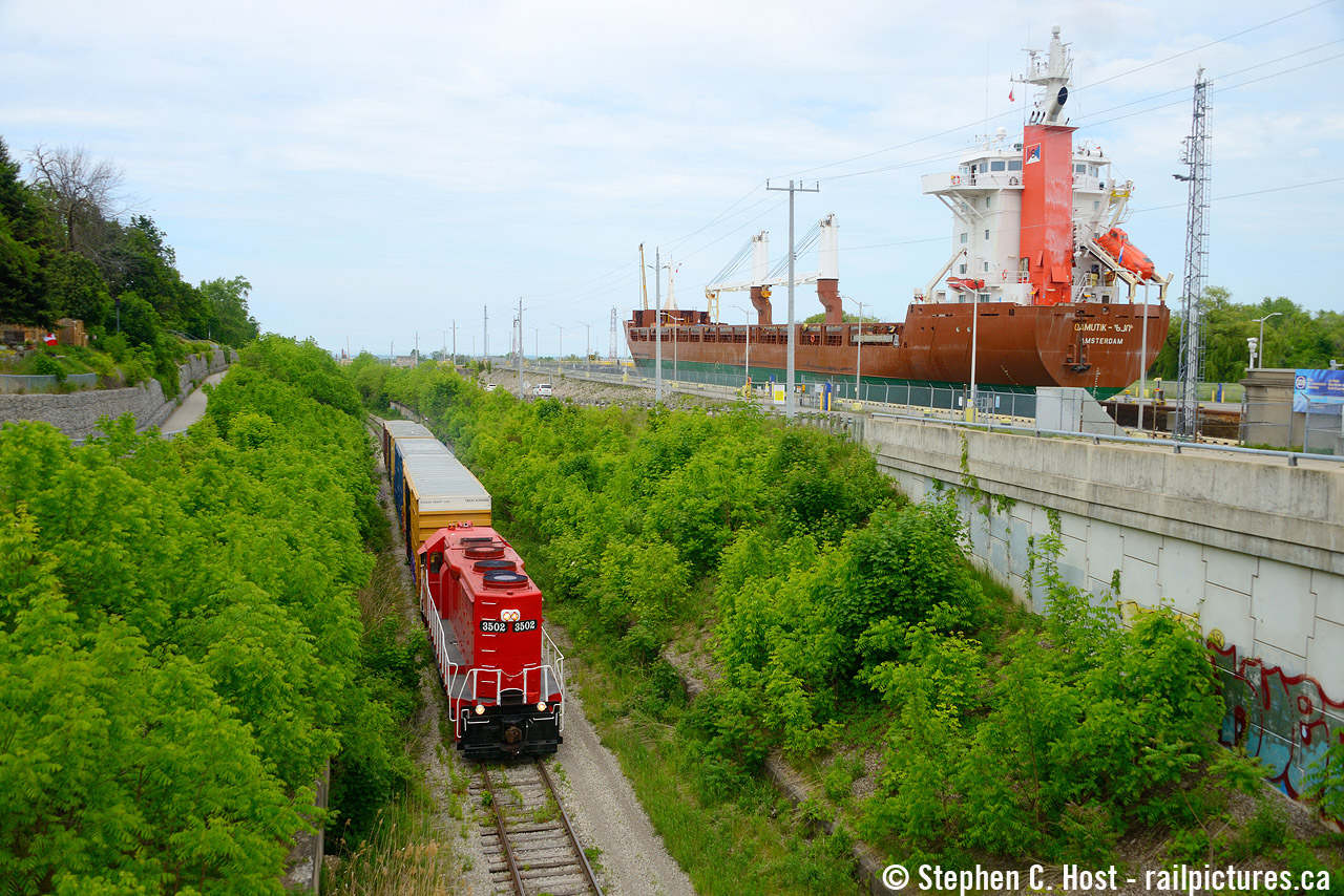 Trillium Railway (GIO Rail) southbound on the Canal sub with empties from Clearwater Paper of St. Catharines. To the right,  MV Kamutik enters lock 7 of the Welland Canal enroute to Iqaluit Nunavut in the far far north of Canada, a journey that will take over a month.