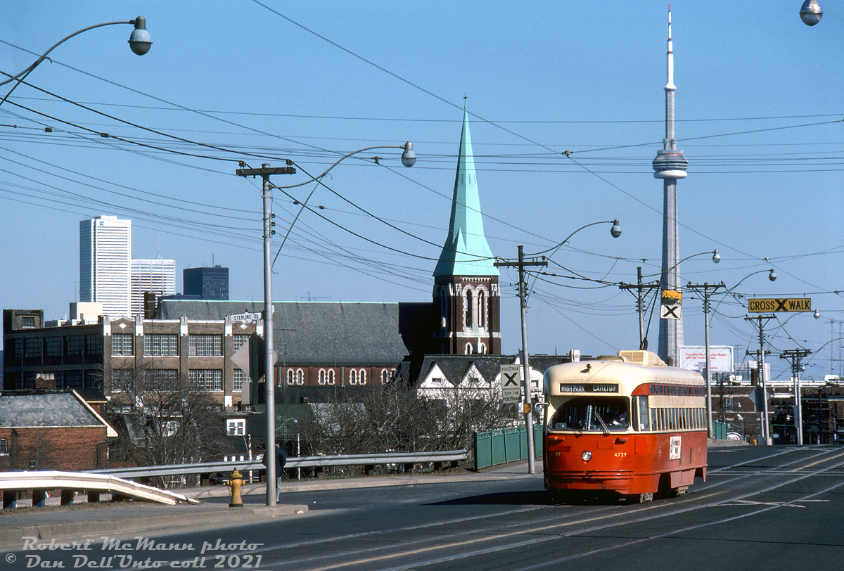 TTC PCC 4729 (an A13-class car originally built new by Pullman in 1947 for Birmingham, Alabama) ambles westbound on Dundas Street West on the Carlton route bound for High Park Loop, seen here at Sterling Road after crossing the CN Newmarket Sub overpass.Markers of Toronto's downtown core are visible in the distance: BMO's First Canadian Place, the TD Centre towers, and most notably the brand-new CN Tower, that would officially open to the public in June. The church in the background is St. Helen's Parish (originally built in 1909) in the Little Portugal area at Dundas & St. Clarens.Robert D. McMann photo, Dan Dell'Unto collection slide.