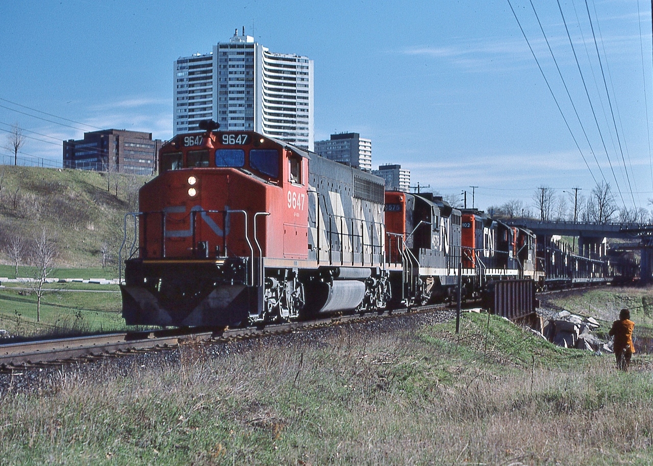 Following Via CN train #98, Northland – due into Union at 08:00 – a CN transfer, Extra 9547,  for Oakville rolls through the Don Valley,


   powered by GMD 1976 built GP40-2(W) #9647 and three GP9's: GMD 1956 built GP9 #4575, GMD 1967 built GP9 #4102, and sister #4523, with empty bi level auto rack CN#710218 first up in the moderately sized consist.


   At mile 6 Bala Subdivision, 7:50 a.m. April 23, 1977 Kodachrome by S.Danko ( with John Baker on the right)


  Question, for those in the know: the GP40W appears to be sans dynamic brakes, the Geep 9's are equipped with dynamics: do non dynamic brake units have a controller to allow the engine man to operate other dynamic equipped units in the MU lashup? 


   First capture of that day: 
 

       classic FP7-A's  


   sdfourty