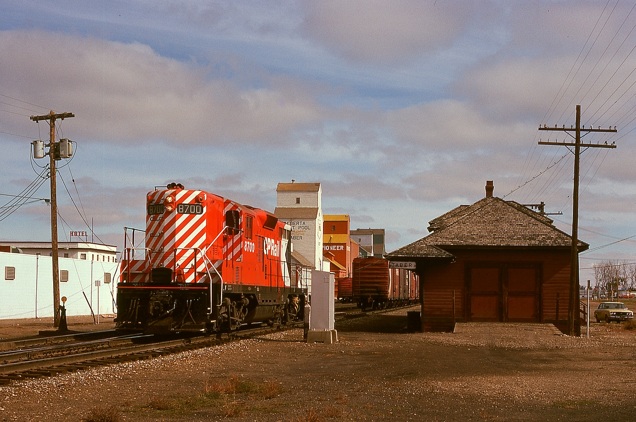 In Taber, Alberta, 2/3 of the way between Medicine Hat and Lethbridge, the hotel in the distance in this shot survives, as the Palace Hotel at the corner of 47 Ave. and 53 St., and the CP main track remains, but the locomotive and depot and distant elevators have all gone off into history.  Here, on Monday 1974-09-30, the daily westward wayfreight No. 83 with GP9 8700 has paused at the depot for switching instructions.