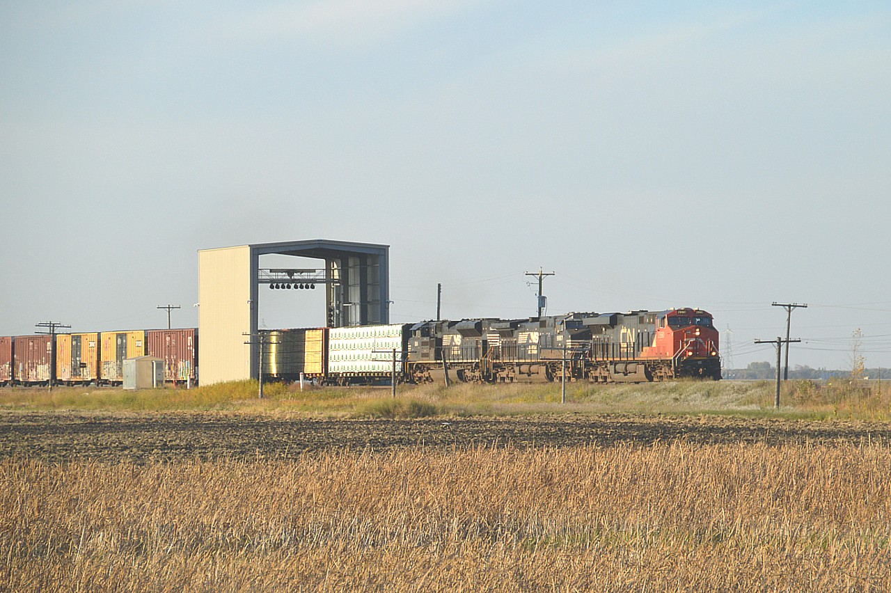 Well, here is something different. An Automated Car Inspection Portal.
This curious looking box-like structure is located about a mile west of the village of Ste Anne in Manitoba. It is one of two in operation; the other being in Winnipeg.
The machine is filled with LED lights and high-definition cameras that instantly capture a 360 degree view of each car as it rolls thru at track speed; around 60 MPH. Rather than manual inspection of rail cars that can take a couple of hours each by CN employees, this machine does the job in seconds, picking out any defective cars as the train passes.
Heading toward Fort Frances Ontario from CN's Winnipeg Symington Yard is eastbound CN 2990, NS 9887 and 1214.