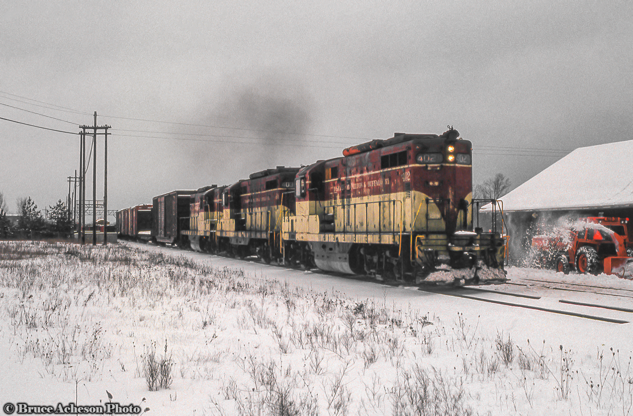 The entire TH&B GP9 fleet can be seen in this shot powering the Starite westbound past Burlington West station.  A CN pow is busy at right keeping the platform and parking lot clear for passengers.
