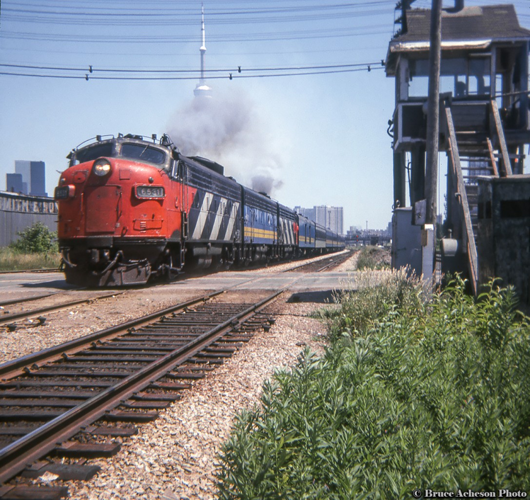 'The Canadian' is seen throttling up on it's way out of Toronto, headed for the Newmarket Sub connection at Parkdale, crossing Strachan Avenue by the watchman's tower with a mix of CN painted GM units bracketing the VIA painted B unit.  CN units were transferred to VIA's roster at startup in 1978.
 At this time the gates at Strachan Avenue, protecting the double track Weston Sub, double track CP Galt Sub, and multiple leads into CP's Parkdale Yard were still manually operated.  I wonder if the steam era bell was still mounted on the east side of the tower by this time?  In the background at left, the planing mill of the John B. Smith & Son Lumber Company  still stands.  The company had been located on this site from 1888 to 1967, when the building took on other uses for various tenants.  Today the old planing mill structure remains as Strachan House (est. 1996), supportive housing, and the name is still faintly on the south side of the building seen here.  In the distance at right the CPR Tecumseh Street Tower can be seen.
VIA 6531, built as CN 6531 in May 1957 and transferred to VIA March 31, 1978, sold to Algoma Central as 1755 in 1995, sold in 2003 to Pioneer Rail and assigned to the Gettysburg Scenic Railroad until 2020.  Purchased by the Potomac Eagle excursion group to be used o their trips out of Romney, West Virginia.  Still numbered 1755 and retaining her Algoma colours.CP switcher action at Strachan Avenue.