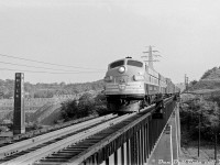 Nearly new Canadian Pacific FP9 1415 and a sister unit lead a passenger train southbound down the Don Branch in 1954, crossing the "Half-Mile Bridge" spanning the winding Don River and CN Bala Sub on the approach to Don Station further south, and on to Union Station downtown via the Toronto Terminals Railway trackage. On the left is the quarry of the famed Don Valley Brick Works (note the cable shovel at the top of the pit), and one of the four smoke stacks for the brick kilns. This photo was taken from one of the larger platforms located in the middle of the bridge (a tedious walk on an active rail line high above a valley with no railings!) <br><br> There was no description included with this black and white negative, but the location wasn't hard to discern at first glance. For the date, 1415 was built in May 1954 as part of an 11-unit order of GMD FP9's for CP's new upcoming transcontinental passenger train "The Canadian", and by December most had rooftop icicle breakers including 1415, so the exact date lies somewhere in between, likely Spring-Summer. Judging by the baggage cars and express reefers on the head end, this is possibly overnight Montreal-Toronto train #21, which according to a September 1954 CP passenger timetable departed Montreal's Windsor Station at 11pm the previous evening, was scheduled to stop at Leaside at 7:08am, and is due downtown at Union for 7:25am. <br><br> The Don Branch between Leaside and Don (beginning of TTR territory) opened in 1892 as part of the Oshawa Subdivision and was CP's main connection to downtown Toronto's Union Station for its passenger trains arriving from and departing to Ottawa, Montreal, and other points east, both via the Oshawa Sub (renamed Belleville Sub) and the Havelock Sub. As passenger service decreased in the 1960's its importance diminished, but the Don Branch did continue to host freight trains travelling to/from Parkdale Yard via downtown, as well as locals, transfers, and detours. The CP and later VIA Dayliner (Budd RDC) passenger service to Havelock also continued to use the Don Branch until the January 1990 cuts. <br><br> One of the last movements on the Don Branch was Canadian Pacific's Holiday Train in December 2007. The line was removed from service 2008, and quietly sold to GO Transit/Metrolinx in 2009 to be "railbanked" for any potential eastern corridor commuter service to Peterborough via the Havelock Sub, or to Oshawa via the Belleville Sub. Various proposals have been floated over the years, but none to date have come to fruition. Meanwhile, city-dwelling Torontonians have taken to using the abandoned Don Branch as a scenic walking trail (without the risk of any 89mph-geared maroon & grey FP9's bearing down on them halfway across). <br><br> <i>Original photographer unknown, Dan Dell'Unto collection negative (large-format scanned with a DSLR).</i>