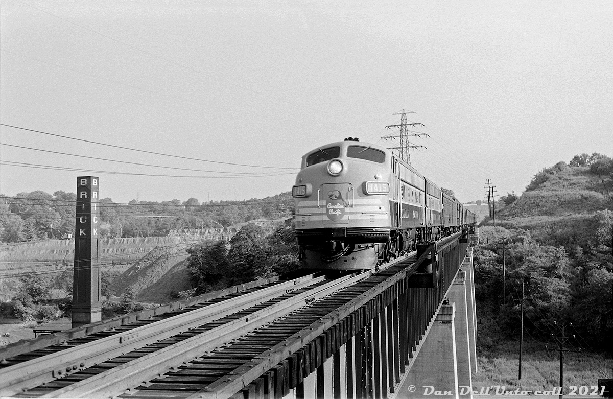 Nearly new Canadian Pacific FP9 1415 and a sister unit lead a passenger train southbound down the Don Branch in 1954, crossing the "Half-Mile Bridge" spanning the winding Don River and CN Bala Sub on the approach to Don Station further south, and on to Union Station downtown via the Toronto Terminals Railway trackage. On the left is the quarry of the famed Don Valley Brick Works (note the cable shovel at the top of the pit), and one of the four smoke stacks for the brick kilns. This photo was taken from one of the larger platforms located in the middle of the bridge (a tedious walk on an active rail line high above a valley with no railings!)  There was no description included with this black and white negative, but the location wasn't hard to discern at first glance. For the date, 1415 was built in May 1954 as part of an 11-unit order of GMD FP9's for CP's new upcoming transcontinental passenger train "The Canadian", and by December most had rooftop icicle breakers including 1415, so the exact date lies somewhere in between, likely Spring-Summer. Judging by the baggage cars and express reefers on the head end, this is possibly overnight Montreal-Toronto train #21, which according to a September 1954 CP passenger timetable departed Montreal's Windsor Station at 11pm the previous evening, was scheduled to stop at Leaside at 7:08am, and is due downtown at Union for 7:25am.  The Don Branch between Leaside and Don (beginning of TTR territory) opened in 1892 as part of the Oshawa Subdivision and was CP's main connection to downtown Toronto's Union Station for its passenger trains arriving from and departing to Ottawa, Montreal, and other points east, both via the Oshawa Sub (renamed Belleville Sub) and the Havelock Sub. As passenger service decreased in the 1960's its importance diminished, but the Don Branch did continue to host freight trains travelling to/from Parkdale Yard via downtown, as well as locals, transfers, and detours. The CP and later VIA Dayliner (Budd RDC) passenger service to Havelock also continued to use the Don Branch until the January 1990 cuts.  One of the last movements on the Don Branch was Canadian Pacific's Holiday Train in December 2007. The line was removed from service 2008, and quietly sold to GO Transit/Metrolinx in 2009 to be "railbanked" for any potential eastern corridor commuter service to Peterborough via the Havelock Sub, or to Oshawa via the Belleville Sub. Various proposals have been floated over the years, but none to date have come to fruition. Meanwhile, city-dwelling Torontonians have taken to using the abandoned Don Branch as a scenic walking trail.  Original photographer unknown, Dan Dell'Unto collection negative (large-format scanned with a DSLR).