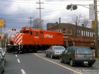 Fresh red paint cuts through the gloomy November atmosphere in Hamilton, as 2-month old rebuilt CP GP7u 1686 handles a local over the Belt Line Branch, making its way through the grade crossing in the intersection of Main Street & Gage Avenue as motorists patiently wait to proceed. <br><br>CP 1686 is no stranger to Hamilton: she was originally built as Toronto, Hamilton and Buffalo 76, one of a 3-unit TH&B GP7 order built by GMD London in 1953 (units 75-77). When CP took over the TH&B in the 80's, they kept running most of the Geep fleet until major failures slowly sidelined them. According to an article in the TH&B <i>Ontarian</i> newsletter by a Mr. Stowe, TH&B 76 was stored out of service in 1984 due to main generator failure, and parked at the CP's John St. roundhouse in downtown Toronto with other sidelined sister units (stored there to keep them from being picked over for parts by CP shop forces). CP's motive power department had approved the units to be rebuilt as yard units as part of CP's 10 Year Motive Power Plan, and all were sent to Montreal to be cycled through Angus Shops for rebuilting in 1987-88. TH&B 76 was outshopped in September 1987 as CP 1686, and assigned to Hamilton as its first assignment. The local crews probably appreciated the new paint, new chop-nose, upgraded electronics and more reliable 16-645C engines (567C engine blocks upgraded with 645 power assemblies).<br><br>When the new GP20C-ECO program started culling the CP GP7/9u herd over two decades later, 1686 was tied up at Moose Jaw SK and retired in May 2012 (just shy of 60 years old), and presumably ended up scrapped.<br><br><i>Reg Button photo, Dan Dell'Unto collection slide.</i>