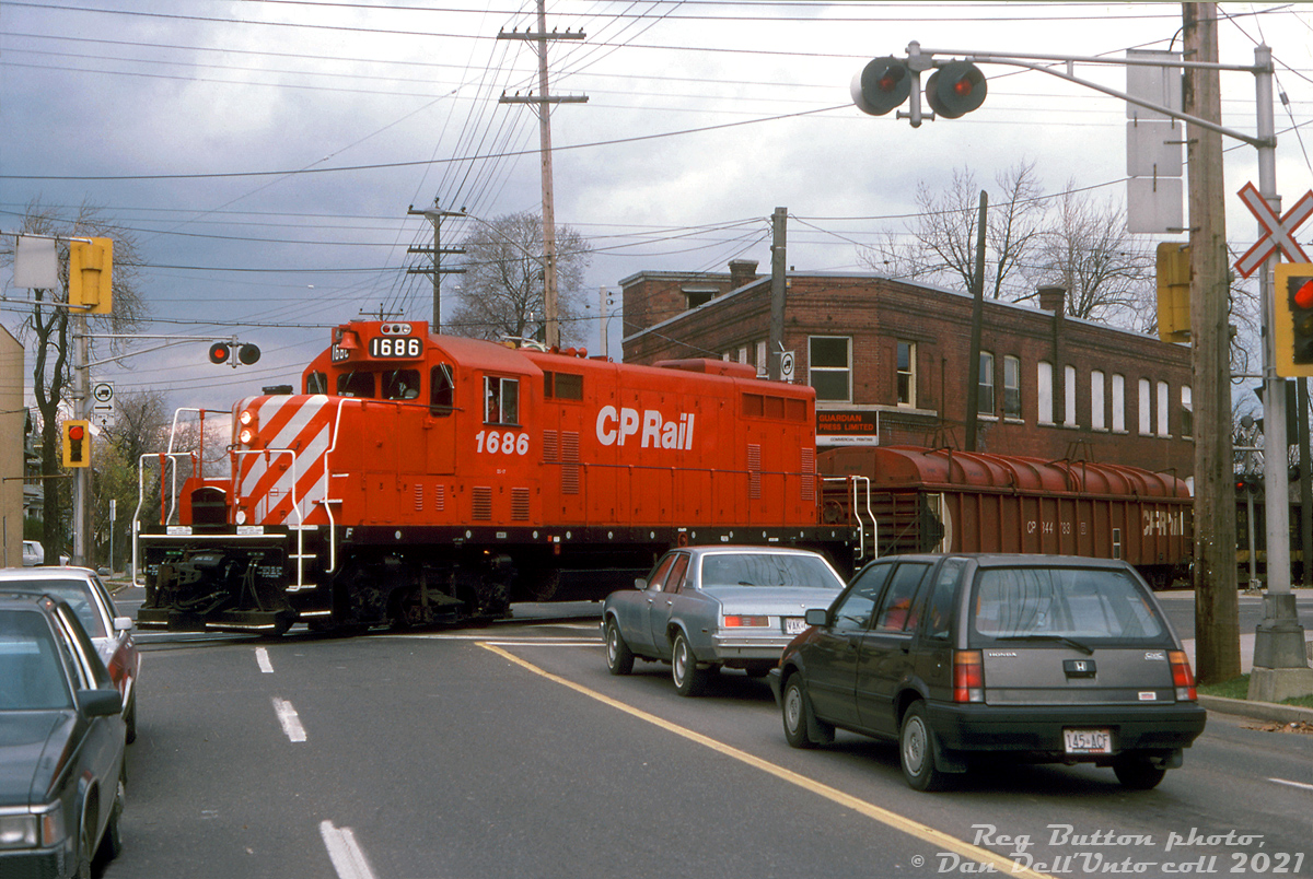 Fresh red paint cuts through the gloomy November atmosphere in Hamilton, as 2-month old rebuilt CP GP7u 1686 handles a local over the Belt Line Branch, making its way through the grade crossing in the intersection of Main Street & Gage Avenue as motorists patiently wait to proceed. CP 1686 is no stranger to Hamilton: she was originally built as Toronto, Hamilton and Buffalo 76, one of a 3-unit TH&B GP7 order built by GMD London in 1953 (units 75-77). When CP took over the TH&B in the 80's, they kept running most of the Geep fleet until major failures slowly sidelined them. According to an article in the TH&B Ontarian newsletter by a Mr. Stowe, TH&B 76 was stored out of service in 1984 due to main generator failure, and parked at the CP's John St. roundhouse in downtown Toronto with other sidelined sister units (stored there to keep them from being picked over for parts by CP shop forces). CP's motive power department had approved the units to be rebuilt as yard units as part of CP's 10 Year Motive Power Plan, and all were sent to Montreal to be cycled through Angus Shops for rebuilting in 1987-88. TH&B 76 was outshopped in September 1987 as CP 1686, and assigned to Hamilton as its first assignment. The local crews probably appreciated the new paint, new chop-nose, upgraded electronics and more reliable 16-645C engines (567C engine blocks upgraded with 645 power assemblies).When the new GP20C-ECO program started culling the CP GP7/9u herd over two decades later, 1686 was tied up at Moose Jaw SK and retired in May 2012 (just shy of 60 years old), and presumably ended up scrapped.Reg Button photo, Dan Dell'Unto collection slide.