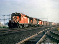 CP Rail GP35's 5012, 5007 and another 5000-series sister unit (either 5010 or 5020) roll an easbound freight along the Belleville Sub through the Leaside area of Toronto, passing by industrial leads and sidings at the east end of the yard. All three sport the new CP Rail branding, including action red paint, 5" end striping and "multimark" logos introduced two years later in 1968 (but repaints didn't generally start until mid-1969). Long an industrial center in the city, today in Leaside most if not all of the rail customers are gone, and the industrial leads and sidings have all been pulled up. What remains of Leaside Yard is a shadow of its former self. <br><br> The 2,500 horsepower GP35 model was the next iteration of EMD/GMD's mid-1960's second generation 4-axle diesel road unit after the GP30, and designed to compete with the likes of GE's U25B and Alco's C424/425 offerings. It sold quite well to US buyers, although Canadian buyers had relatively newer fleets at the time so didn't purchase all that many: CP went in for two GP30's, and three subsequent GP35 orders (that only amounted to 24 units total). Some were purchased new, others were purchased through EMD/GMD's trade-in program using old or wrecked power such as GP7's, FP7's, F7B's, etc and some components from them were reused. CN only purchased two GP35's and followed up with 15 GP40's, and later many many more GP40-2L/W units. <br><br> The GP35 model wasn't favoured by CP motive power officials, as problems cropped up with them over time and GM was reportedly resistant to working on fixes. More complex transition and wheel slip systems, more DC brushes to change in the main generators, and reliability issues (many argue the 567-block was being was being pushed to its limits by then at 2500 horsepower) didn't play in their favour, and CP de-rated them down to 2250hp at one point. Years later when they were assigned out west, a few Port Coquitlam shop employees took them under their wing and worked out many of the bugs, improving performance. Most were retired and sold off in the 90's, with a few becoming cab control units 1125-1128 (some still on the roster today) paired with GP38-2's. <br><br> <i>Original photographer unknown, Dan Dell'Unto collection slide (duplicate)</i>