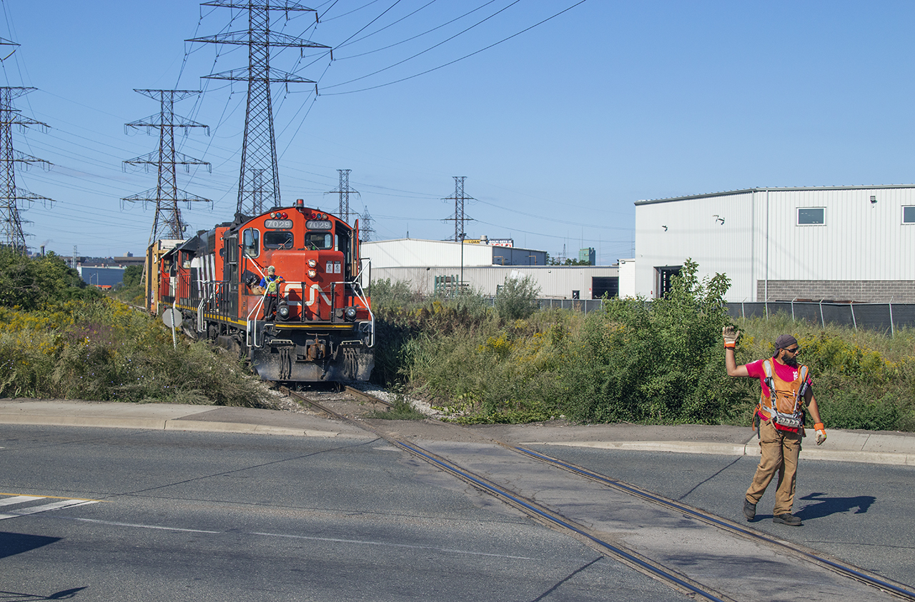 The conductor on the 0700 job has the crossing protected and waves his partner, who is controlling the movement, to come ahead.  Once clear of the road they will spot the box at Parkdale Warehousing before proceeding over to Railcare.