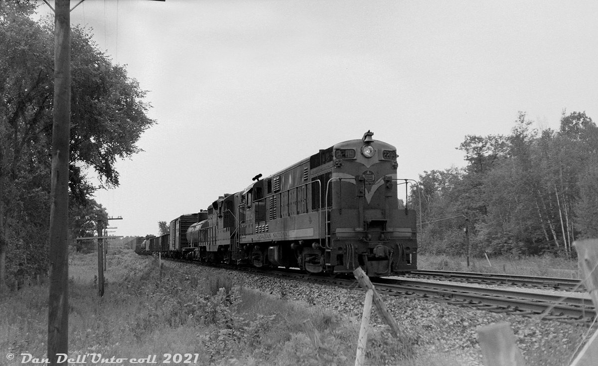 Canadian National 2209, one of CN's handfull of CLC H16-44 units, leads a GP9 on a northbound freight on the Bala Sub rolling through Sparrow Lake in Ontario's "Cottage Country" during July 1962. Sparrow Lake proper was located at mile 93.9 of CN's Bala Sub (north of Washago, near the southwest point of its namesake lake), although this photo was likely taken to the south at the crossing by Port Stanton Parkway and South Port Sparrow Lake Road.

During the early rush to dieselization, the Canadian Locomotive Company of Kingston, Ontario was licensed to manufacture and sell Fairbanks-Morse locomotive designs in Canada. CN and CP were their main Canadian customers, taking multiple orders in the 1950's to build up their new diesel fleets and banish steam. CN purchased 4- and 5-axle C-Liners, H16-44's, a lone H24-66 "Train Master" unit, and some smaller offerings including H10-44, H12-44 and oddball H12-64 models. They differentiated from the competition by using Fairbanks-Morse's opposed-piston diesel engines, a well-regarded design popular in marine use.

2209 was one of 18 H16-44 units CN purchased from CLC in 1955, first numbered 1841-1858 and later renumbered 2200-2217. Unlike most of CP's fleet of FM-CLC units that were based out of the west, CN's C-Liners and H16-44's were based in the east, and ran mixed with other equivalent models from competitor GMD and MLW pulling mainline freight and passenger trains in Ontario, Quebec, Eastern Canada and (early on) Vermont. CN's H16-44 units were also set up to run long hood forward, like most of their hood units at the time.

As the 1960's rolled around, FM-CLC had exited the locomotive market, and oddball first generation locomotives fell out of favour on most Canadian and US railroads. Most mainline FM-CLC units ended up retired and traded in or scrapped during this period (some were bought by marine supply outfits for their opposed-piston engines). CN's FM-CLC fleet was retired during the mid-late 1960's, and many of the stripped carbodies ended up in the scrap lines at London and Montreal awaiting the final indignity from the torch. CP's lasted a few years more until the bulk of their fleet were retired during 1975.

Original photographer unknown, Dan Dell'Unto collection negative (large-format scanned with a DSLR).
