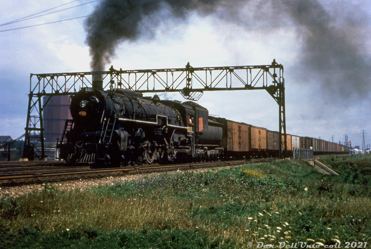 It was mentioned that some of the old steam-era signal bridges in the Union Station Rail Corridor were due to be changed out by Metrolinx soon (late 2021). So here's some steam-era 1950's Toronto Terminals Railway action: Canadian National U3a "Northern" 6303 heads westbound under the signal bridge at Parliament Street subway/viaduct with a long freight in tow, on the approach to Toronto's Union Station downtown. Another signal bridge is visible in the distance at Cherry Street, by the namesake interlocking tower and Don Yard. The train will be diverting to the "High Line" at Scott Street interlocking tower and bypass Union's train shed and inbound tracks. Wooden ice reefers trail on the head end, possibly bound for the icing facilities at Mimico Yard. The round tank-like structure in the background is a gasometer at Consumers Gas Plant A (Parliament & Front), one of three of their coal gas facilities in Toronto.

CN 6303 was one of a handful of Grand Trunk Western 6300-series 4-8-4 Northerns sent north of the border to parent Canadian National (some sources indicate during WW2). Built by Alco at Scenectady NY in July 1927, 6303 would serve out her final years operating out of CN's Mimico Roundhouse alongside CN's own Northerns before being retired at the end of the steam era, and eventually scrapped in July 1961.

Original photographer unknown (duplicate slide), Dan Dell'Unto slide collection.

Some Bill Thomson CN 6300 photos:
CN 6300: http://www.railpictures.ca/?attachment_id=28667

CN 6301: http://www.railpictures.ca/?attachment_id=13305