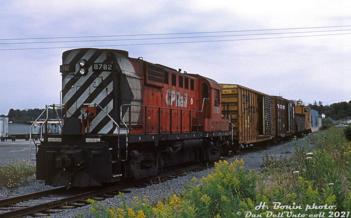 CP RS18 8782 sits with a short train on the spur serving the CP Express terminal in Kingston, Ontario. The main warehouse (note loading docks, cars were spotted on the main spur) and truck trailers can be seen in the background. There was also a siding to the west for a loading platform/ramp track. The main spur branched off the CP Kingston Subdivision, and continued east past here and curved north to serve the nearby Superior Propane dealer. By this point in time, less than a year remained for CP's remaining operations in Kingston.Not to be confused with CN's more well-known Kingston Subdivison, CP's Kingston Sub was originally built as the Kingston & Pembroke Railway in the 1870's, running from Kingston's downtown waterfront north to Renfrew. Like many early lines, the K&P was absorbed into Canadian Pacific, and the line became CP's Kingston Subdivision. Over the next few decades the line would be abandoned in sections from the early 1960's until the final 35-mile section from Tichborne (off the CP Belleville Sub) to Kingston was abandoned in 1986.The CP Express terminal in Kingston was located along the south side of Dalton Avenue west of Division Street, in the northeast part of town near Highway 401. It had been relocated here from a downtown waterfront location in 1967, and was served off a spur from the CP Kingston Subdivision. When CP abandoned the Kingston Sub and left town, CN continued to serve at least Superior Propane via their Queens North Spur, connecting to a short section of former CP track via a switchback to access both sites (it's questionable if the CP Express terminal was ever served by CN during this time). Today, everything has been redeveloped into a large commercial plaza.Hughes Bonin photo, Dan Dell'Unto slide collection.Further References:The City of Kingston has some good aerial imagery showing the line here (the 1970, 78, 90 and 98 maps offer interesting views). As always, for anything and everything Kingston rail-related, Eric Gagnon's Trackside Treasures has more info on CP's customers in Kingston.