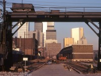 Preface: a photo exemplifying the slow decline of the railway's importance to the downtown cores of Toronto and other big cities. Once the main method to reliably transport both people and goods across Canada and into the US, the shift of manufacturing out of downtown to the suburbs and overseas, the transition from blue-collar to white-collar employment (traditional manufacturing giving way to business/finance/commerce/technology sectors of the economy, often centralized in major North American cities such as Toronto and Montreal), changing modes of transportation including the rise of truck traffic, globalization, containerization, airline travel and the private automobile meant the railways didn't really factor in as prominently in many people's lives as before, or in the operations of many of the "new" downtown businesses (other American cities were less fortunate, as historically the rise and move to the suburbs often left downtowns desolate and crime-ridden. This fate was largely avoided by Toronto and other large Canadian cities). <br><br> As such, railways followed where their customers went: sidings to new suburban business parks, new modern automated classification yards outside of the cities where land was cheap and plentiful, new piggyback and container-handling yards located near major highways and junction points, and centralized freight sorting/logistics warehouses. Demolition of many old steam-era railway facilities in and around downtowns followed, many by now either outdated, under-utilized, constrained for space, or replaced by newer facilities. CN and CP both came up with redevelopment plans for their sprawling downtown real estate holdings. The CN Tower, for instance, was just one part of a larger 70's Metro Centre development plan that never came to fruition. Even Toronto's Union Station was considered for demolition and redevelopment at one point. <br><br> -------------- <br><br> Framed in the Whiting 20-ton overhead crane over the nearby team tracks, the old CP Express / Dominion Express Company freight sheds and office building at Simcoe and King Streets are slowly being reduced to rubble, in preparation for redevelopment as a new concert hall site for Massey Hall. Originally built in 1912-13, the sidings in the distance running along the sheds and platforms were once home to long cuts of 40' boxcars taking in and unloading LCL (Less than Carload) shipments, transloaded to/from teams of horse-drawn wagons and later trucks for local dispersal. Steam engines and early diesel switchers would regularly head up the King Street shed lead's incline from Bathurst Street, cross Spadina and head to the sheds to pull and spot cuts of boxcars, as was also the case at CN's own freight sheds located to the south (demolished around 1967-68). We're looking east from Peter Street towards the main site, bounded by King, Simcoe, Wellington and John Streets (upper-most yard in the middle <a href=http://jpeg2000.eloquent-systems.com/toronto.html?image=ser12/s0012_fl1967_it0027.jp2><b>here</b></a>). The main CP Express offices were in a <a href=http://www.railpictures.ca/?attachment_id=30801><b>7-story building</b></a> at the SW corner of King & Simcoe (partially visible) that will also be demolished (there were some who voiced opposition to demolition of the office and proposed incorporating it into the new development, and the city did recognize its historic value, but ultimately it was not saved). The orange backhoe on the roof and equipment in other photos suggests local demolition contractor Teperman Wrecking is doing the work, also known for demolishing the old Eaton's Queen Street store. <br><br> New modern office towers loom high in the background, pointing to future trends to come for downtown Toronto. The new development coming here is a joint effort between CP's real estate branch Marathon Realty, who wanted multiple office towers with commercial space, the City of Toronto (spearheaded by mayor David Crombie) who wanted to incorporate a certain amount of housing under a new planning board requirement, and the Massey Hall board of governors who wanted a site to build a new Massey Hall concert venue. Initially the project was sparked by a request from Mayor Crombie to CP CEO Ian Sinclair about using the site for a new Massey Hall. Sinclair agreed and got CP's real estate arm Marathon involved. According to a July 1976 article in the Toronto Star, after much negotiation (CP was opposed to incorporating housing in the then-still industrial area) a deal was worked out between the three parties, but some viewed the land lease terms the city agreed to as very favourable for Marathon. Maybe too favourable, as even though the plan was voted on and accepted by city council, there was some debate about it: one member quipped it was "the worst deal since Sir John A. Macdonald sold part of Canada to the railways for two pieces of steel", others considered it a "total sell-out" on the mayor's part to Marathon. <br><br> At any rate, the old freight sheds and office building were demolished in the late 70's, the site was cleared, and development on the new Massey Hall began. The name was changed to Roy Thomson Hall because of a donation from the Thomson family during fundraising efforts, and the new concert venue opened for the Toronto public in September of 1982.  <br><br> Despite the initial agreement, other new development on the site was slow to follow, and most of the property (and adjacent former CN land to the south) remained parking lots for years until more development began in the late 80's. Notable was Metro Hall, a new office building for the pre-amalgamation Metro Toronto governing body, that would be built on the site in 1992. Some of the old CP freight sheds on the right of the photo (west of John Street) and team tracks would be retained into the mid-1980's for paper deliveries (the "Paper Shed"), but they too were eventually demolished after 1987. <br><br> One small piece did manage to elude the wrecking ball: the old crossing shanty in the middle of the photo for the John Street grade crossing (John St. intersected part of the sidings and sheds, and was manually protected) would be saved, and today is preserved at the TRHA's Roundhouse Park nearby. <br><br> <i>Keith Hansen photo, Dan Dell'Unto collection slide.</i>