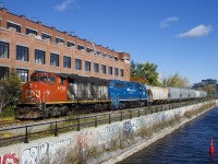 CN 4795 & GMTX 2257 are pushing seven grain loads towards Ardent Mills (mostly obscured by trees in this view) as they pass the heavily tagged retaining wall of the Lachine Canal.