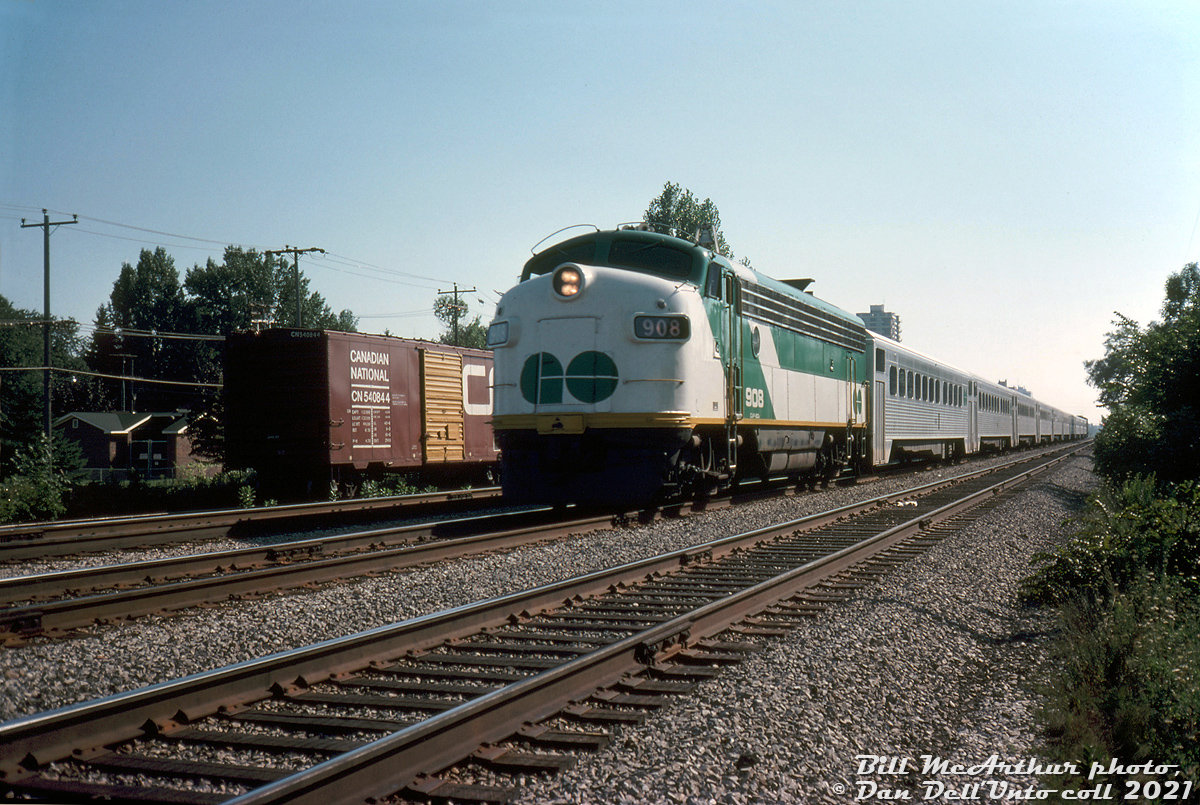 Only a year into her second career, GO Transit APCU 908 hustles eastbound through Port Credit East on the CN Oakville Sub with a train of 10 Hawker Siddeley single-levels and GP40-2W 706 pushing on the rear. Built as Ontario Northland FP7 1511, the unit was part of the second group of F's converted for GO Transit in 1975 as non-powered cab car/HEP generator cars for use at one end of commuter trains, with a non-HEP equipped GP40-2W locomotive at the other end.

CN 540844 sitting on the service track to the south was one of CN's numerous 40' steel boxcars built in the 1950's, a later variant with larger 8' doors to facilitate easier forklift loading with cargo such as newsprint rolls. The yellow doors were a CN colour-coded signifier: initially introduced on cars intended for handling higher class merchandise, before being more commonly associated with newsprint service cars.

Bill McArthur photo, Dan Dell'Unto collection slide.