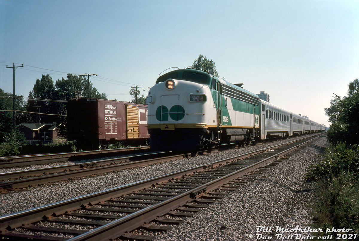 Only a year into her second career, GO Transit APCU 908 hustles eastbound through Port Credit East on the CN Oakville Sub with a train of 10 Hawker Siddeley single-levels and GP40-2W 706 pushing on the rear. Built as Ontario Northland FP7 1511, the unit was part of the second group of F's converted for GO Transit in 1975 as non-powered cab car/HEP generator cars for use at one end of commuter trains, with a non-HEP equipped GP40-2W locomotive at the other end.

CN 540844 sitting on the service track to the south was one of CN's numerous 40' steel boxcars built in the 1950's, a later variant with larger 8' doors to facilitate easier forklift loading with cargo such as newsprint rolls. The yellow doors were a CN colour-coded signifier: initially introduced on cars intended for handling higher class merchandise, before being more commonly associated with newsprint service cars.

Bill McArthur photo, Dan Dell'Unto collection slide.