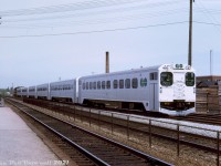 <i><b>Inbound from Toronto</b></i>: GO cab car C753, one of the original numbers assigned to the cab car fleet (later becoming GO 9853, and then 103), pulls into Oakville Station at the end of its westbound run on the Lakeshore corridor. After a brief pause for passengers on board to de-train and new passengers to board the consist of six single-level Hawker Siddeley cars, the 600-series GP40TC on the other end will lead the train back east for Toronto and Pickering.<br><br>In the distance, CN SW1200RS 1237 sits on the north service track east of Trafalgar Road, no doubt handling switching duties. Small industries were once plentiful and dotted along the sides of most rail lines. On the right are Main Lumber and Monsanto Canada, both located southeast of the station off Trafalgar, and both with their own rail sidings. The powerlines for Trafalgar Road cross overhead while the roadway crosses underneath the rail corridor at a matching angle.<br><br><i>Original photographer unknown, Dan Dell'Unto collection slide.</i>