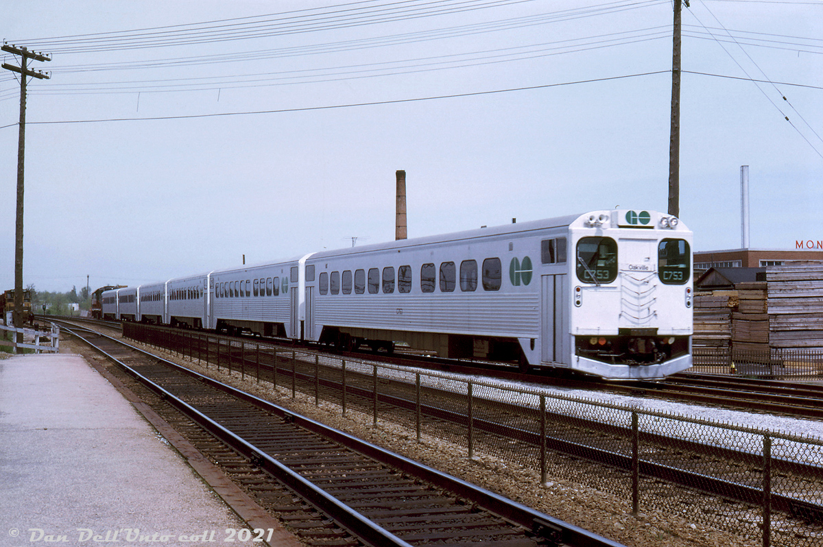 Inbound from Toronto: GO cab car C753, one of the original numbers assigned to the cab car fleet (later becoming GO 9853, and then 103), pulls into Oakville Station at the end of its westbound run on the Lakeshore corridor. After a brief pause for passengers on board to de-train and new passengers to board the consist of five single-level Hawker Siddeley cars, the 600-series GP40TC on the other end will lead the train back east for Toronto and Pickering.

In the distance, CN SW1200RS 1237 sits on the north service track east of Trafalgar Road, no doubt handling switching duties. Small industries were once plentiful and dotted along the sides of most rail lines. On the right are Main Lumber and Monsanto Canada, both located southeast of the station off Trafalgar Road, and both with their own rail sidings.

Original photographer unknown, Dan Dell'Unto collection slide.