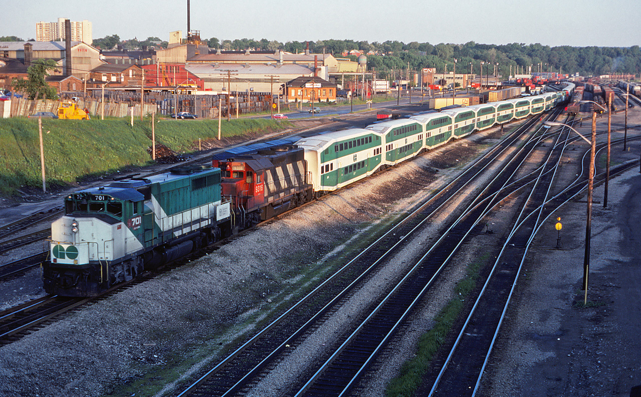 As a follow-up to Mr. Dan Dell'Unto's recent post, here is a different view of a deadhead GO move arriving in Hamilton, two months later. According to the slide mount, this is GO 701 and CN 9316 with APCU 904 on the rear of the first consist, followed by GO 704 and CN 9317 with APCU 906 trailing. Unfortunately, the slide does not include the photographer's name.Just over the roofline of the lead coaches, you can see another cut of those tarpaulin-covered short containers on flatcars. Does anyone know what these are?Dan's post is here:http://www.railpictures.ca/?attachment_id=47239