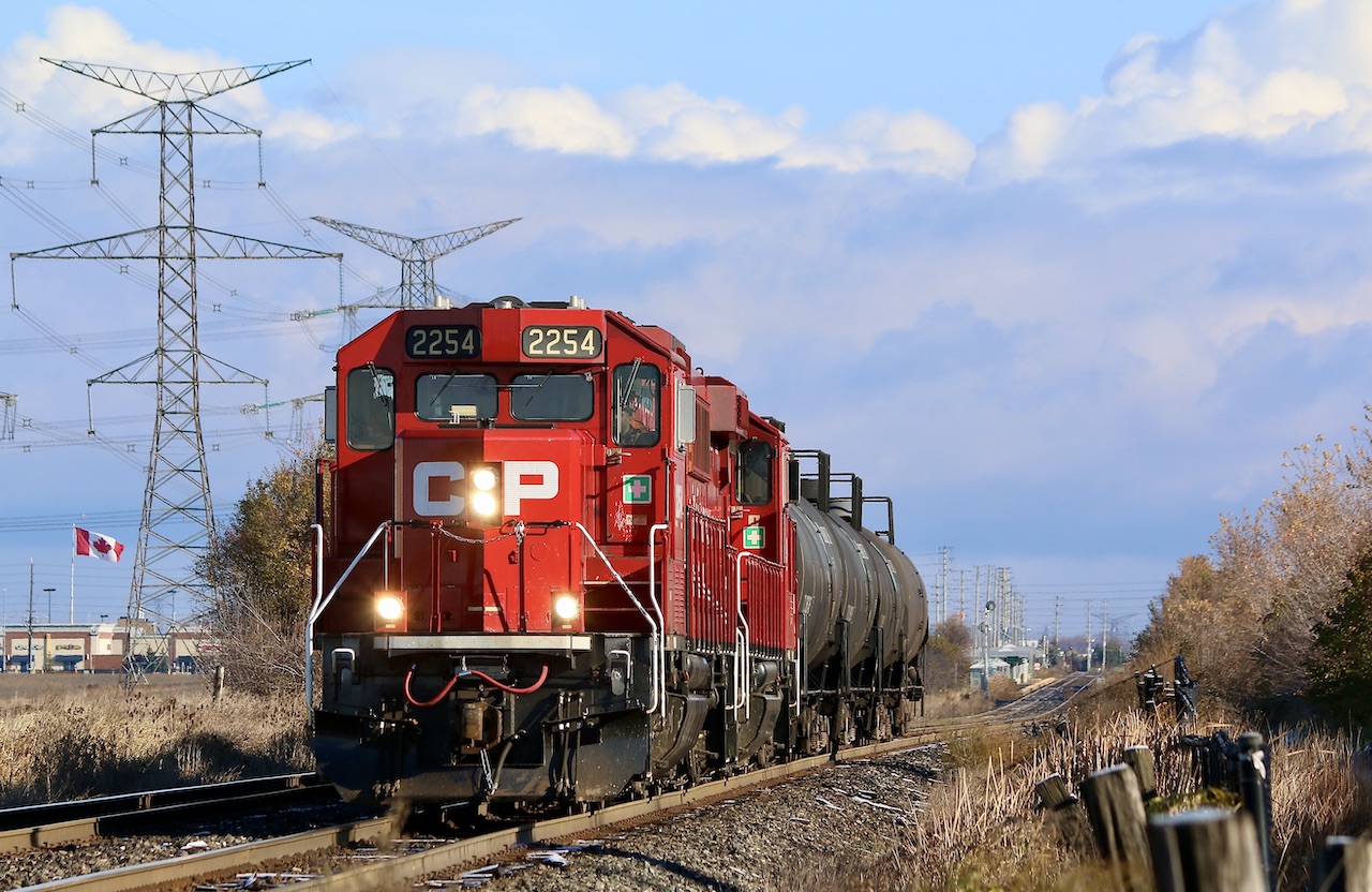 A large Canadian flag flaps in the crisp autumn morning wind as CP T14 stretches its legs over its more recently expanded territory. Over the past month the trains assignments have been expanded to now cover working the former "Expressway" yard in Hornby, now a bulk transfer facility operated by Cando. The train with its two matching GP20ECO's are slowly heading to the west end of the yard to drop a cut of tank cars before returning to the east end to lift another cut of cars before heading back to Streetsville. Lisgar GO station can be seen in the distance.