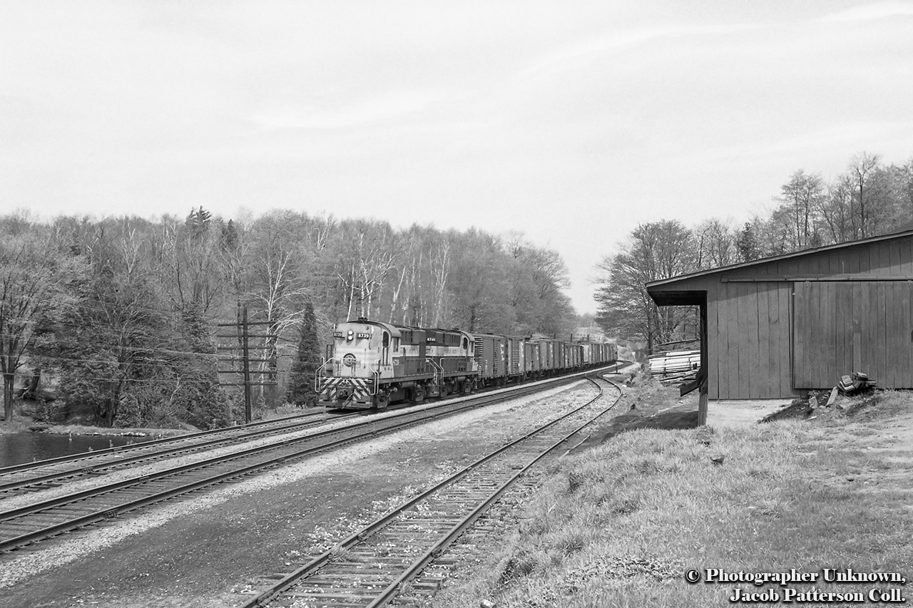 A pair of MLW RS18s, built in 1957, power extra 8739 west upgrade at Campbellville passing the stub track for Crawford Lumber and Fuel, seen at right, and the CPR freight shed, on the west side of Regional Road 1/Guelph Line. Date is approximate.Originally built in 1889 as the Lewis Brother's Brick Works, the property would be purchased by Murray Crawford in 1900, who converted it into a sawmill, later expanding into fuels.  Much of the original mill burnt down in 1957, leaving just the coal sheds and office and warehouse buildings.  Today, these structures remain, though the loading dock seen above is gone.  The coal shed is now a furniture shop, Fine Oak Things, the office serves as Longhaul Logistics, a freight service, and the warehouse building is a Thai restaurant. 
 There is also a former CNR caboose 78337 on the property.Lead unit 8739 would not see the rebuild program in the 1980s, having suffered a wreck at Bath, New Brunswick when hitting a washout about 0300h on April 1, 1976.  One crew member killed.  Parts were salvaged from the locomotive, however due to the difficulty of removing it, the loco was simply buried.  Trailing unit 8741 would be rebuilt in August 1984 to RS18u 1821 and retired from the CP in the mid 1990s.  1821 would be sold to the New Brunswick East Coast in April 1998, sold to CN with the NBEC/OCRR purchase in 2008, and sold again in 2009 to Le Massif de Charlevoix 1821.Bill Thomson's shots from the freight shed, April 25, 1964:CPR 21, "The Chicago Express", approaching the crossing.CPR 21, head end passing freight shed.The tail end for the final time.Original Photographer Unknown, Jacob Patterson Collection Negative.