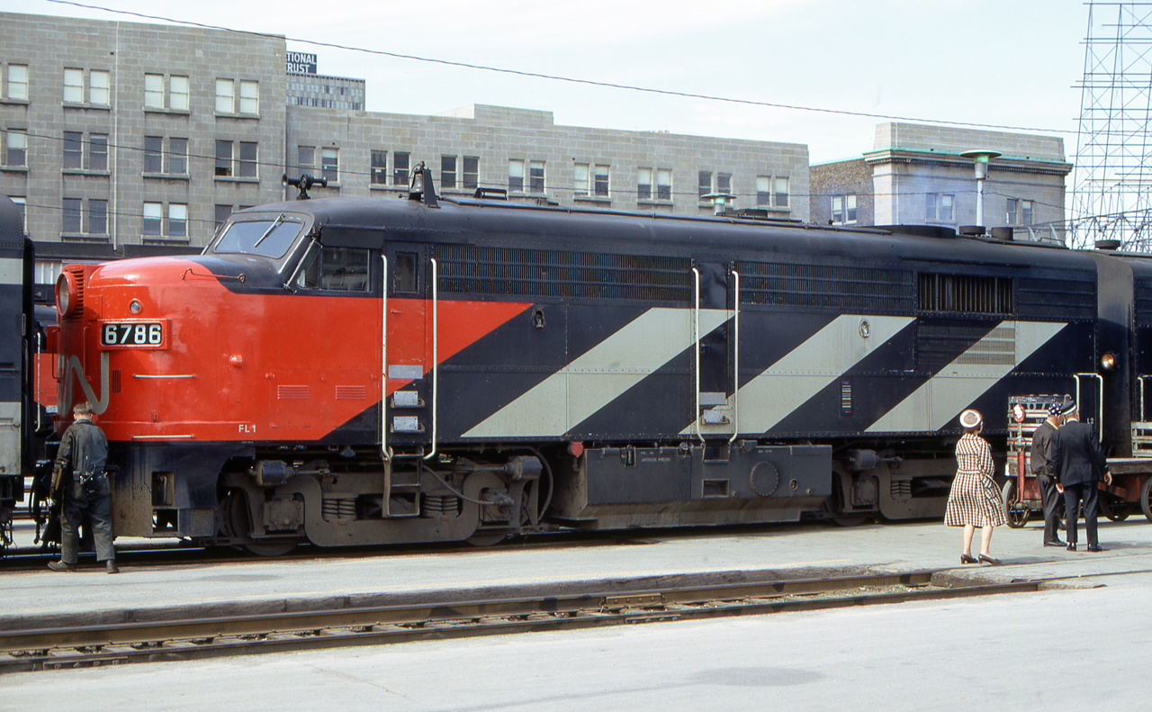 Over the years I have gone out of my way to avoid people in my photos. Yet, when I saw this slide, the people came alive. No longer was this just a sterile front-coupled roster shot of a MLW FPA-4, but this was a small piece of history captured on film.
CN 6786 is at Toronto Union Station in mid-June 1972. A worker is going between the locomotive and the first car. Perhaps he will uncouple the locomotives from the train. Two men (possibly crew members or a railfan and a crew member) are talking at the back end of the locomotive. The woman seems to be getting impatient while waiting for one of the men to stop talking  and to leave with her. The baggage cart reminds me that soon passengers' baggage will be unloaded.
Then I noticed the number of the unit. It was CN 6786. That seemed familiar. On my first railfan trip to Canada in 1968, she was the first MLW FPA-4 I photographed. I was reunited with an old friend!