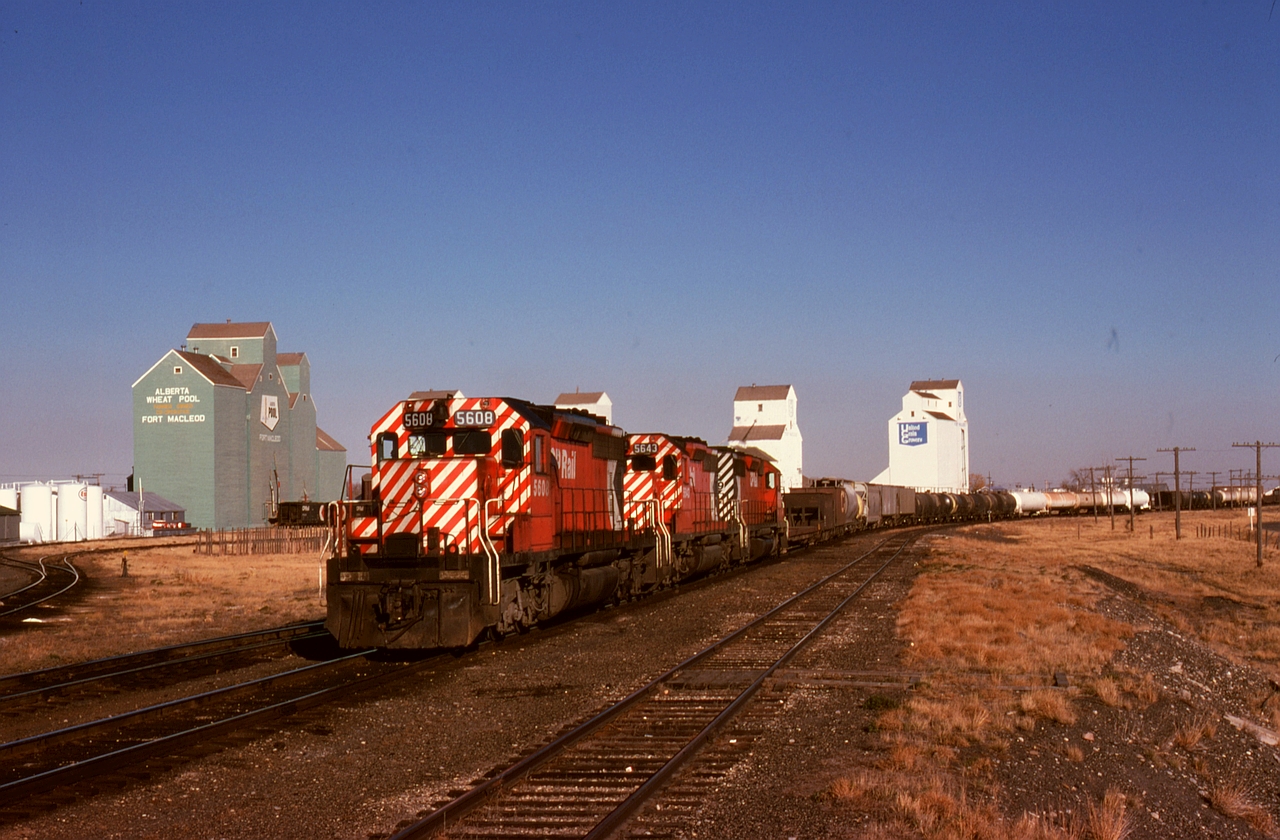 Westward from Lethbridge, train 979 headed with fresh crews at Crowsnest and Cranbrook through to the Union Pacific at Kingsgate/Eastport, shown here approaching the Macleod sub. (now removed) junction at Fort Macleod, with a trio of SD40-2s 5608 + 5643 + 5639 for power.  As may well be imagined, three of those four grain elevators (except the nearest one) are now history.
