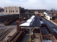 How the mighty have fallen: the decline of the significance of Canadian passenger rail travel is exemplified by this photo of the old 1931 Canadian National Hamilton (James Street) Station, once hosting many <a href=http://www.railpictures.ca/?attachment_id=42983><b>steam-powered passenger trains</b></a> at its platforms, but now mostly relegated to a car repair shop for CN's car department, working on freight cars from the nearby Stuart Street yard and Hamilton industrial area in need of repairs.
<br><br>
Heavyweight 6-axle passenger cars pulled by <a href=http://www.railpictures.ca/?attachment_id=39091><b>Northerns</b></a> have been replaced by beat-up gondolas used for hauling scrap, flatcars, and barrel ore hopper cars used on the Dofasco ore trains from the north. A wheel flatcar is visible at the bottom left, used for hauling new wheelsets to shops and yards for change-outs, and used wheelsets to the scrapper.
<br><br>
The platform on the right with the covered ramp from the station still served what few passenger trains still called on Hamilton at this time. VIA operated about a half-a-dozen Toronto-Hamilton-Niagara Falls RDC runs that stopped here. GO also ran 2-3 rush hour GO trains since the system's 1967 inception, and next year, the joint VIA-Amtrak <a href=http://www.railpictures.ca/?attachment_id=36825><b>"Maple Leaf"</b></a> would start using the station. But by the early 90's, most passenger operations relocated to the new Aldershot Station, and Hamilton Station lay vacant. LIUNA would later convert the station into its present-day use as a venue and banquet hall.
<br><br>
<i>Keith Hansen photo, Dan Dell'Unto collection slide.</i>