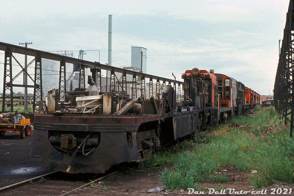 The sad end of CP's Canadian Locomotive Company (Fairbanks Morse) and Baldwin locomotive fleets: the cut-down remains of a CLC C-Liner sits at the end of the scrapping line at Ogden Shops, ahead of a string of Baldwin DS4-4-1000 and DRS4-4-1000 locomotives and another C-Liner, all in the process of being stripped down and eventually cut up. Just a few sandboxes, air tanks, and other components remain above the frame of the lead unit, after the carbody was stripped off and internal components salvaged.

Going by some spotting features, the lead unit appears to have been CP CFA16-4 4057, likely followed by DS4-4-1000 7073, and CPA16-4 4105. The fifth unit is another switcher, 7068, and the other four mixed in are DRS4-4-1000 units 8001-8004 in unknown order (except the final unit, 8004). All were retired in 1975 during the great purge of CLC, MLW and Baldwin power due to a system-wide downturn in traffic.

For those inclined, here's a short history of the two oddball fleets:

The FM/CLC units:

Fairbanks Morse (designs licensed to Canadian Locomotive Company in Kingston for Canadian production) made a name for themselves during dieselization by offering their opposed-piston diesel engines (popular for marine use) in their diesel locomotives, producing more power than the competition with fewer cylinders. They offered a wide range of configurations in their streamlined Consolidation line ("C-Liner"), 4- and 6-axle road switchers (H-series, including the most powerful on the market: their 2400hp "Train Master"), and small switching units. Alas, increased competition, reliability issues and decreased orders saw FM exit the locomotive market in the late 50's. Most railroads gradually repowered or retired their FM/CLC locomotives in the 60's, by that time many considered them oddballs, non-standard or unreliable (at least for railroad use). 

CP kept their fleet going much longer than other roads, mainly in the west based out of Nelson BC and Alyth (Calgary AB). However as the 70's rolled around and newer 6-axle mainline power was purchased, plans were in place to gradually retire the CLC fleet: as units failed or faced extensive repairs they were retired, and as part of the phase-out, regular overhauls were reduced or cancelled. A traffic downtown in the mid-1970's accelerated much of this: CP took a bunch of leasers off-lease, parked most of their MLW 244-powered fleet, and retired most of their CLC and Baldwin units.

The end:

In March 1975, the power desk issued an order to round up all the remaining CLC power, dead or alive, and send it to Ogden for storage (CP's parlance was tied up unserviceable/serviceable). A handful of F-units and GP9's were reassigned to Nelson as replacements (but only lasted a few months before Nelson shop itself was closed in June 1975). This included the fleet of H16-44 roadswitchers, and what few C-Liners remained. The CP C-Liners were the last of their kind operating anywhere in North America, and by 1975 only five units remained in service: 4053, 4057, 4065, 4104 and 4105 (4057 officially retired in March because of a frozen engine block, the rest in June).

There was talk of the monthly cost of maintaining the CLC fleet versus leasers, and plans to keep some of the units stored for possible traffic increases, but ultimately the remaining fleet ended up officially retired June 20th 1975 and subsequently scrapped. Parts off the CLC fleet common to other power (notably MLWs) that CP wanted to reuse were the GE 752 traction motors, air compressors, SKF roller bearings, wheels and axle sets. CP ended up selling roughly two-dozen of the retired unit's engine blocks to an equipment supply company out of Houston TX (as the opposed-piston engines were popular in the secondhand market for marine use). Only three units were spared for preservation: 4065, 4104 and 8554. CP's three remaining Train Masters survived in hump service until they were similarly phased out.

The Baldwins:

The Baldwin fleet was made up of a small handful of DRS4-4-1000 roadswitchers (8000-8012) and DS4-4-1000 switchers (7065-7075), ordered by CP early on to fully dieselize their E&N Vancouver Island operations and the surrounding port area. Because both Alco/MLW and EMD couldn't guarantee production space for CP's order, CLC brokered a deal for Baldwin to produce the 1000 horsepower units, which were built at Eddystone PA. 

Their isolation out west no doubt contributed to their longevity, but by the 1970's they were oddballs and similarly phased out by CP. Four 8000's were wrecked in 1973, and most of the others still active were retired in 1975. Units 8000-8004 (plus 7068 and 7073) were officially retired June 5th 1975, and 8009-8010 in December of that year, but some of the switchers lasted a bit longer (the final unit retired in 1982). 8000 was spared for preservation, but 8001-8004 and the two switchers were cut up here at Ogden.

Original photographer unknown, Dan Dell'Unto collection slide.