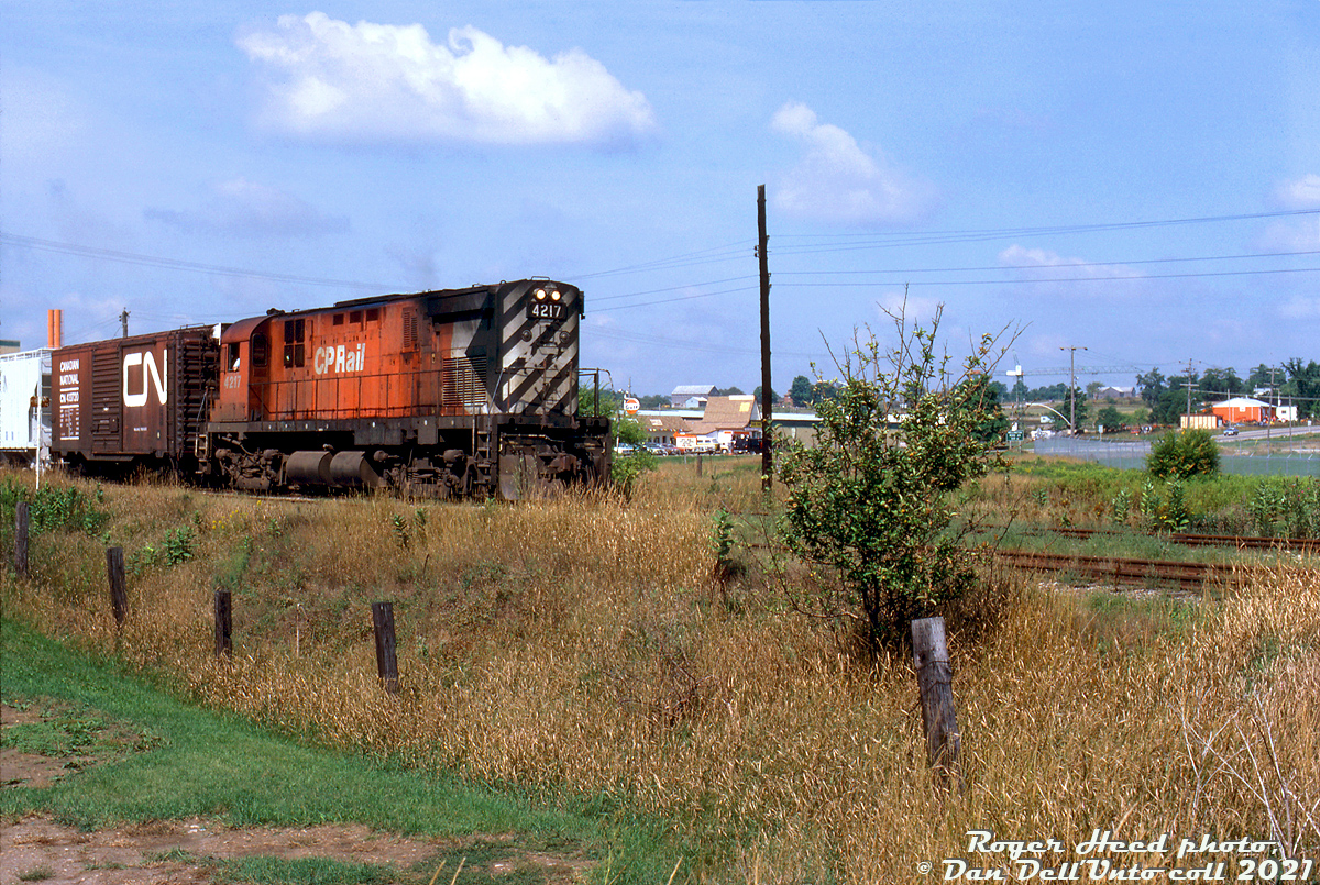 What could be more "Sleepy CP 80's Ontario branchline" than a lone CP C424 running back home long hood forward through a small town?

Sporting white extra flags not relocated from its trip west, CP C424 4217 peddles her wayfreight along the CP Elora Sub heading eastbound through the town of Erin, Ontario. The train has just passed Main Street (Wellington Road 124) and is returning back east to Cataract (and likely on to Orangeville), presumably from Fergus where the trailing CN 40' boxcar may have been lifted from the interchange with CN. Erin was Mile 4.5 of the 29.4 mile CP Elora Sub, which branched off the Orangeville Sub at Cataract (Mile 0) and wound its way through Erin, Hillsburg, Belwood, Fergus to end at Elora.

A 1982 timetable lists the light rail branchline as 25mph maximum speed but with most of the line covered by 20mph speed restrictions. During its final year in 1987, conditions on the line had deteriorated and it was down to 15mph with a number of 5 and 10mph speed restrictions. The all-too-familiar story of low traffic volumes lead to CP abandoning the entire Elora Sub at the end of 1987 (which is now the Elora-Cataract Trailway).

Roger Heed photo, Dan Dell'Unto collection slide.