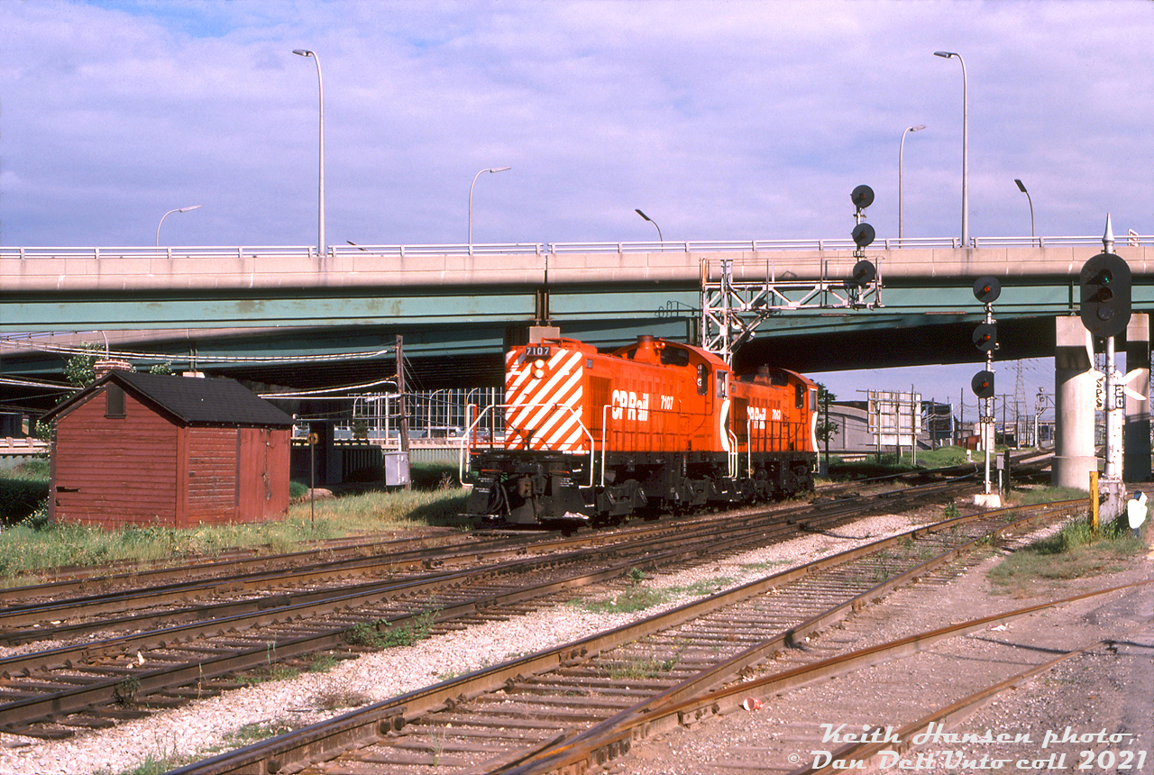 A pair of CP Rail MLW switchers, S4 7107 and S2 7063, hustle their way north up the Don Branch (CP Belleville Sub) past a section house at Don, ducking under the Eastern Avenue bridge spanning the railway corridor and Don River. The trailing unit didn't have MU, so this could be a light power move from John Street north to Agincourt Yard.

The trackage to the right leads across Bayview Avenue to the nearby S. McCord concrete plant (note the neat cutouts on the signal targets to clear rail equipment on the siding). CN's Bala Sub runs in the middle, with crossover tracks visible here allowing CP to cross CN and access the old CN and CP Cherry Street yards in the West Donlands industrial area, that branched out just to the south of here (much still intact at the time, but removed in the 90's). Today the former CP Don Branch sits unused awaiting future GO use, while the Bala Sub next to it sees normal GO and VIA passenger activity.

Keith Hansen photo, Dan Dell'Unto collection slide.